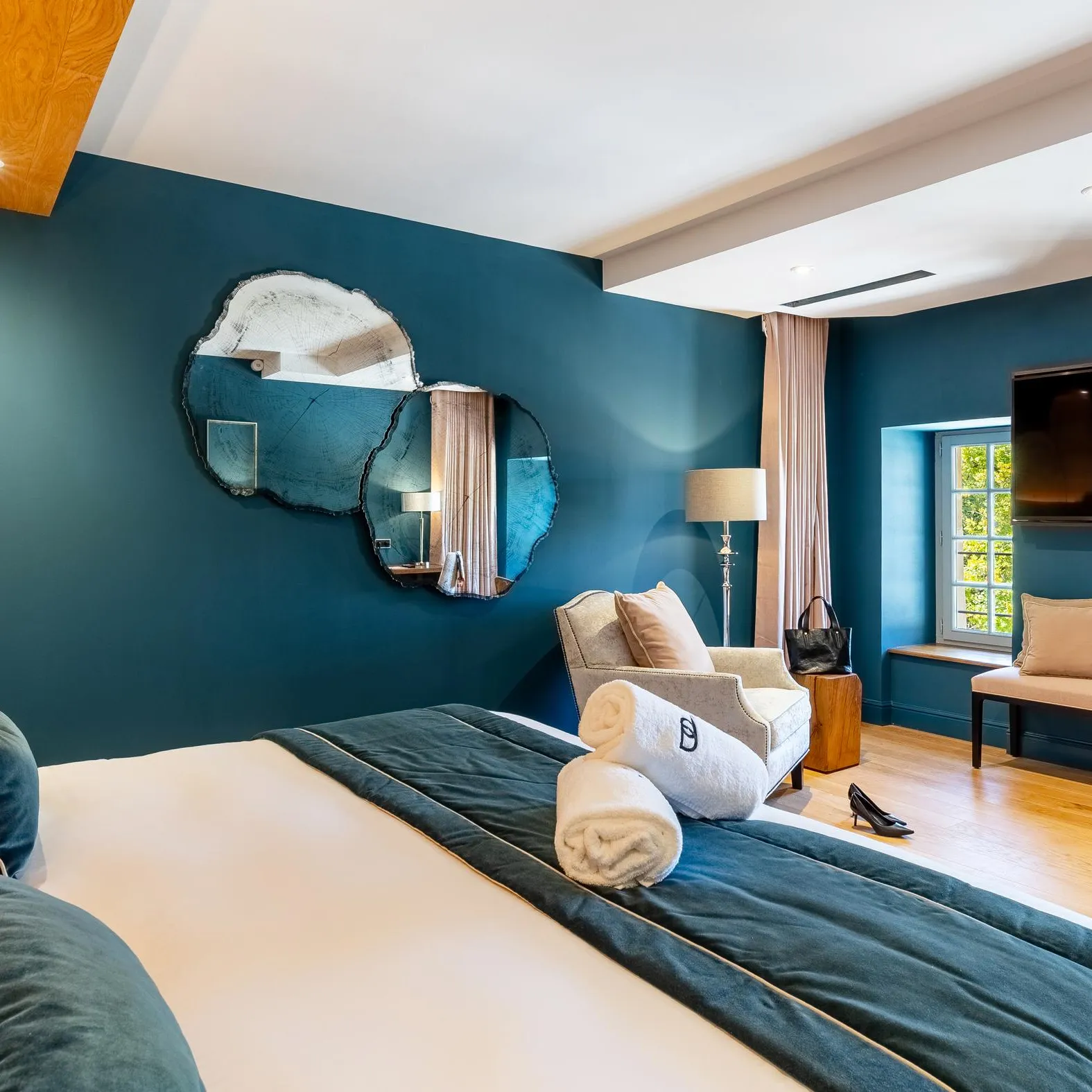 Chambre moderne avec lit, fauteuil, télévision, miroir mural et fenêtres donnant sur l'extérieur