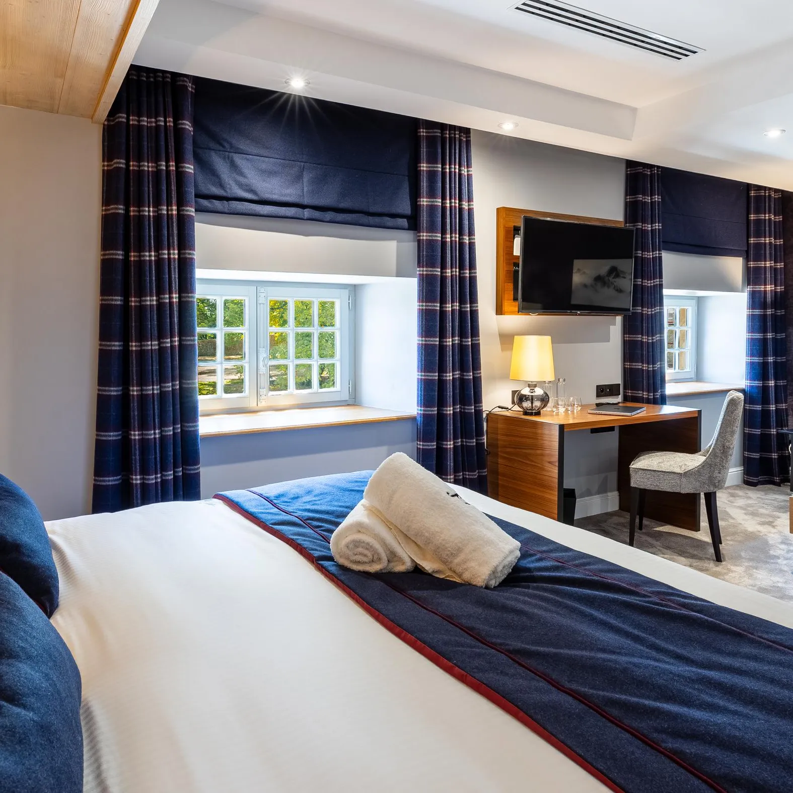 Chambre d'hôtel avec lit double, sofa, bureau, télévision et fenêtres donnant sur un jardin