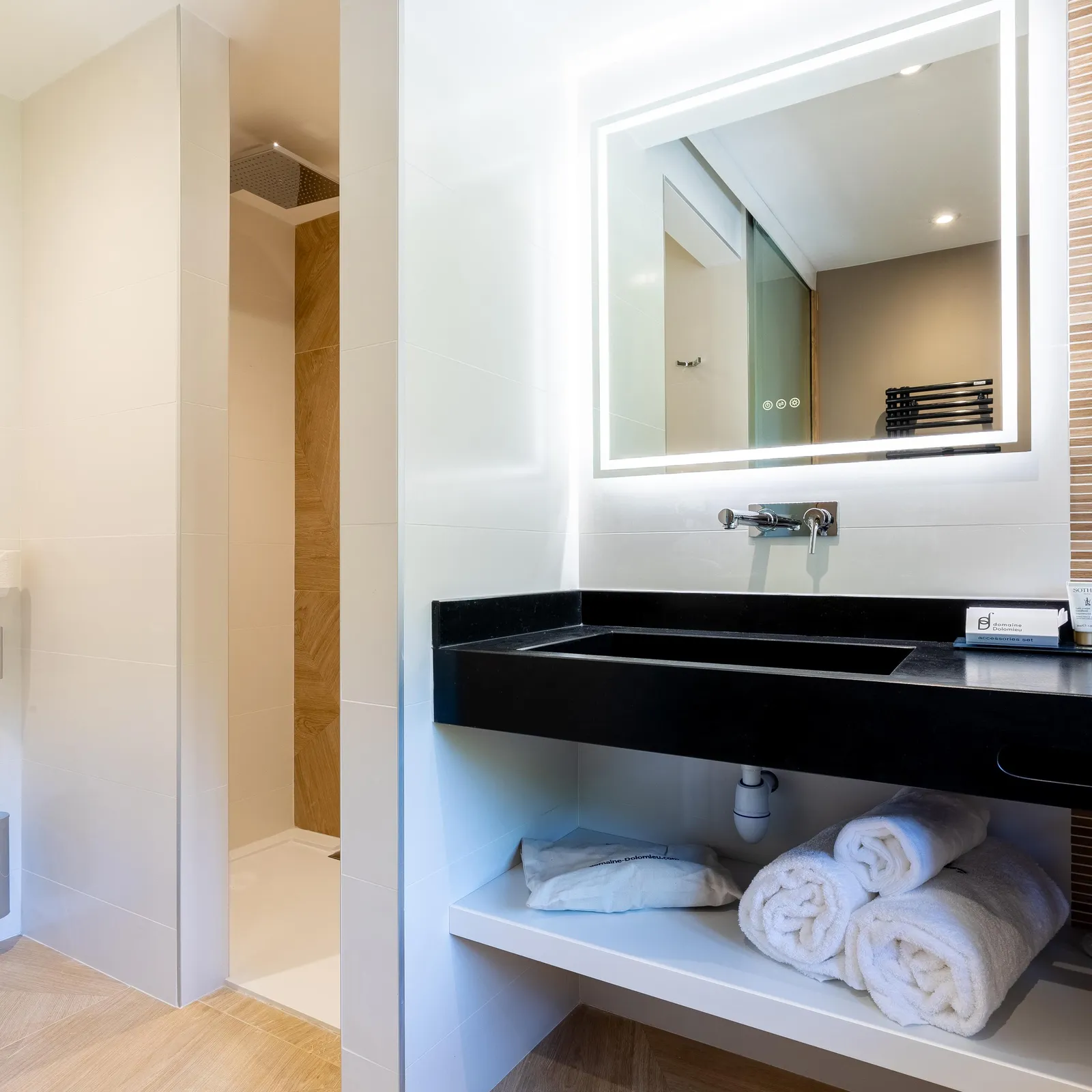 Salle de bain moderne avec lavabo noir, miroir éclairé et serviettes blanches sur une étagère