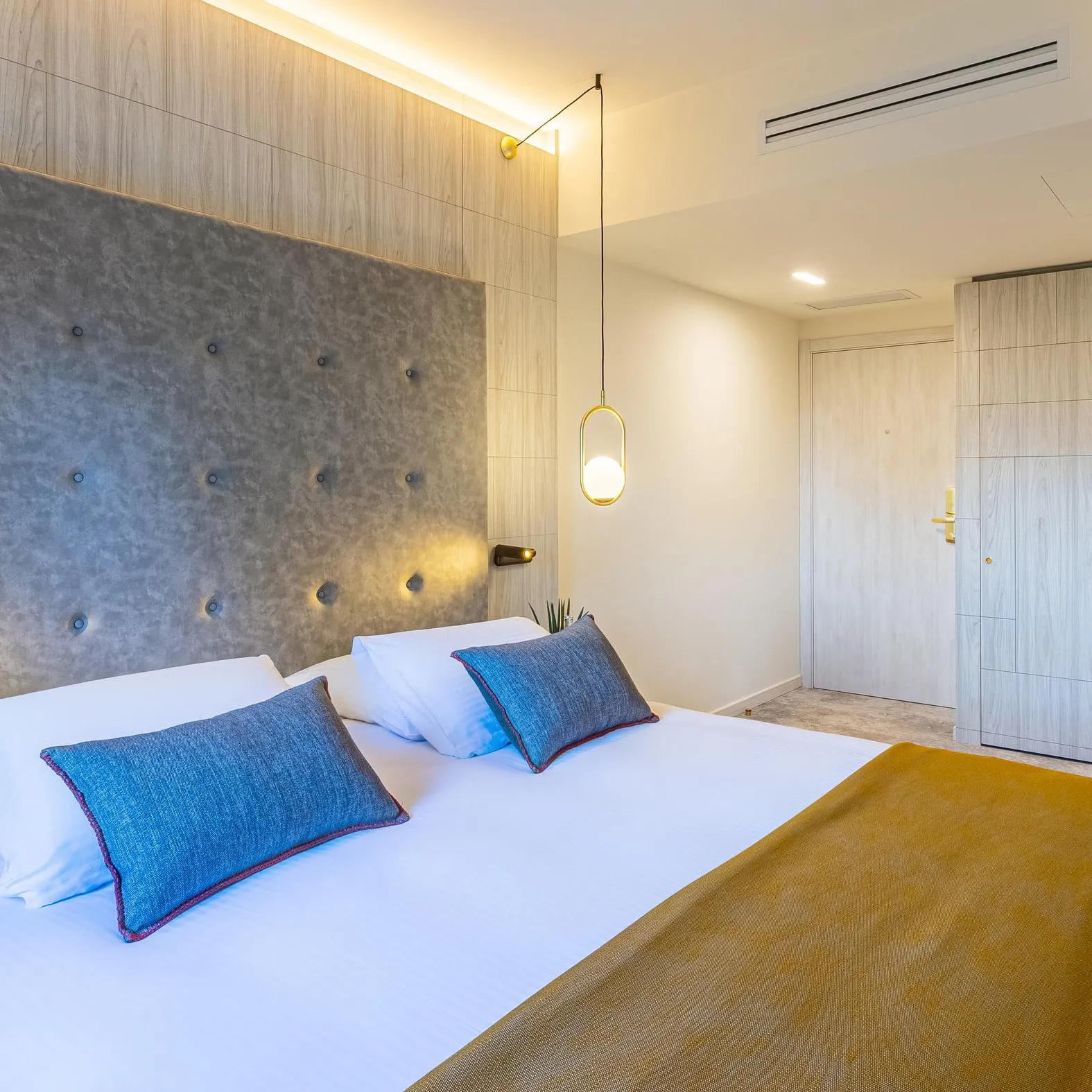 Chambre moderne avec un lit double, des coussins bleus, une tête de lit grise et des armoires blanches