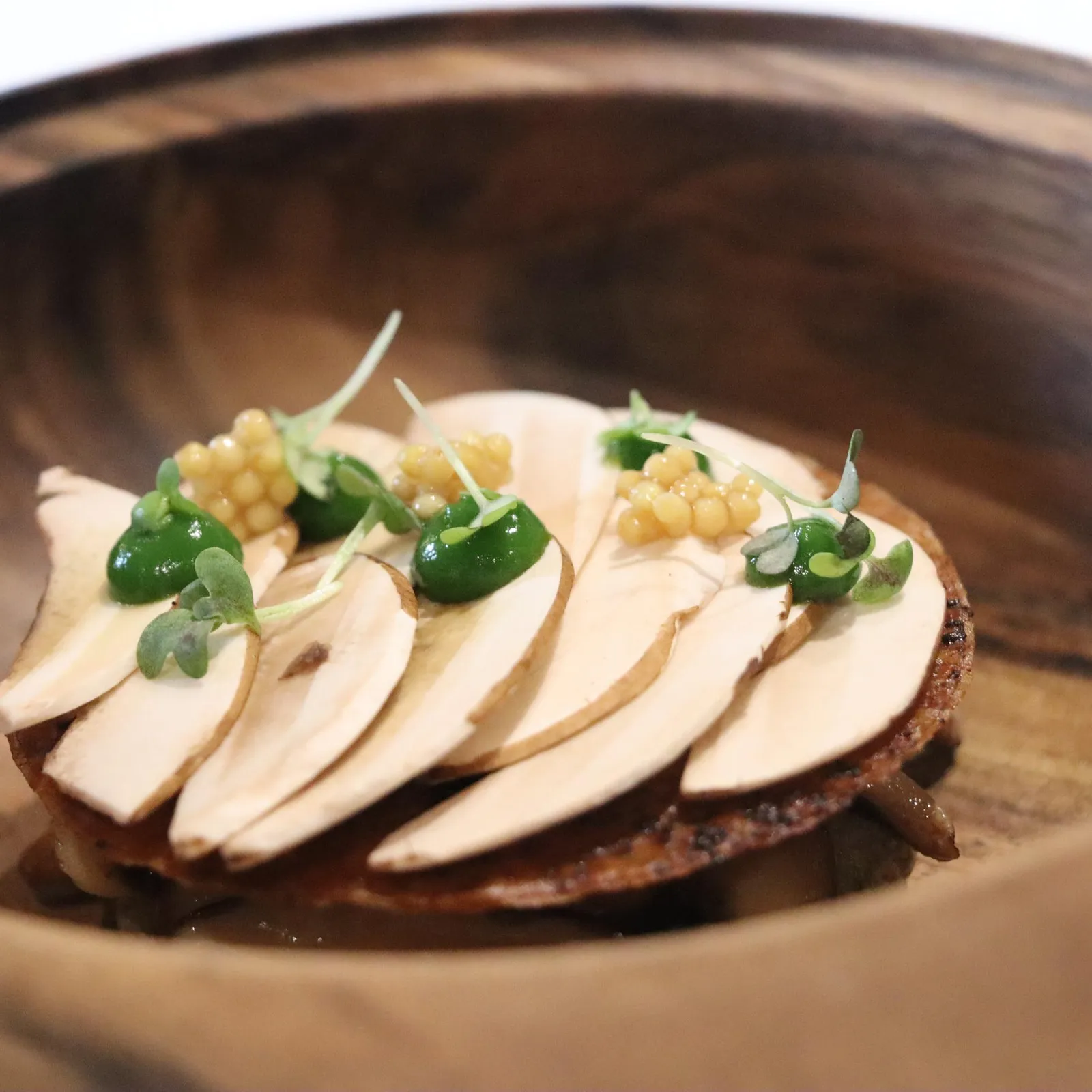 Assiette en bois contenant des tranches de champignons grillés garnies de micro-pousses et de grains jaunes