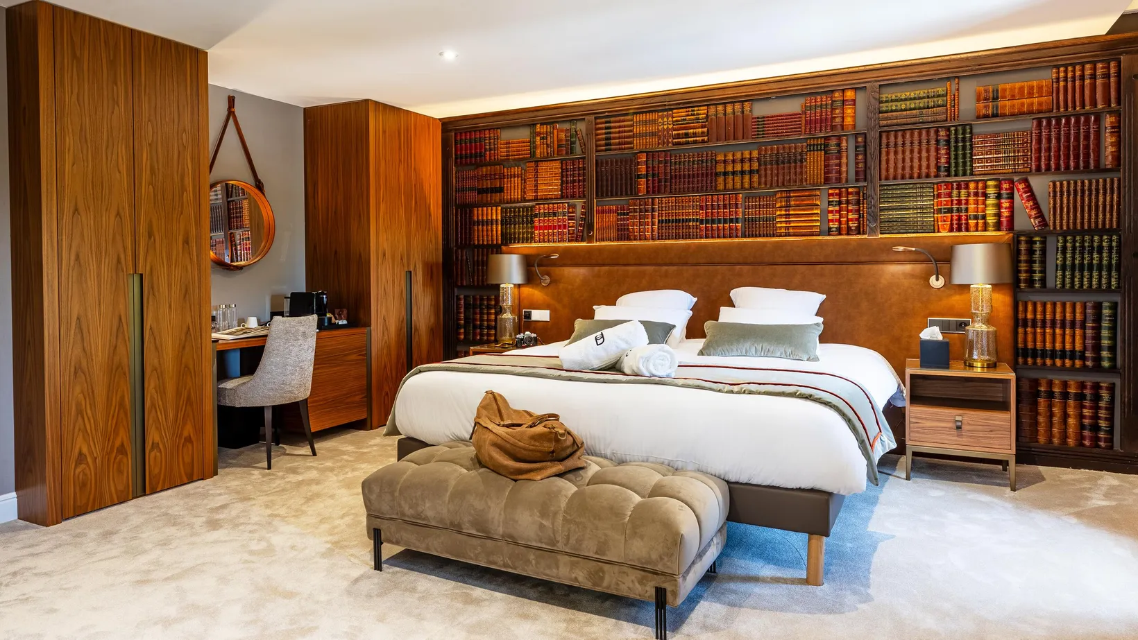 Zimmer mit einem großen Bett, einer Bank am Fußende des Bettes, vollen Bücherregalen und einem Schreibtisch mit einem Stuhl