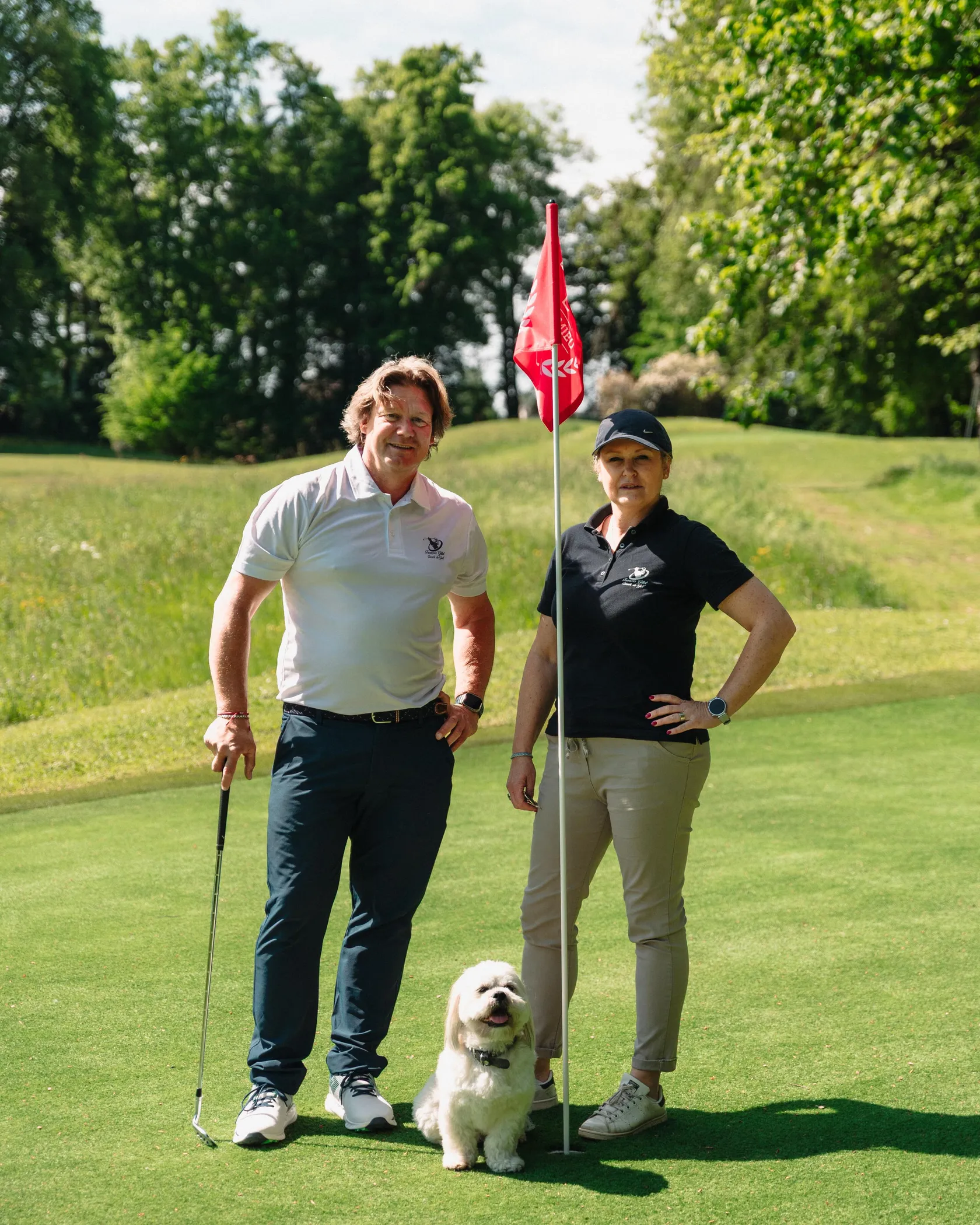 Deux personnes et un chien sur un green de golf près d'un drapeau