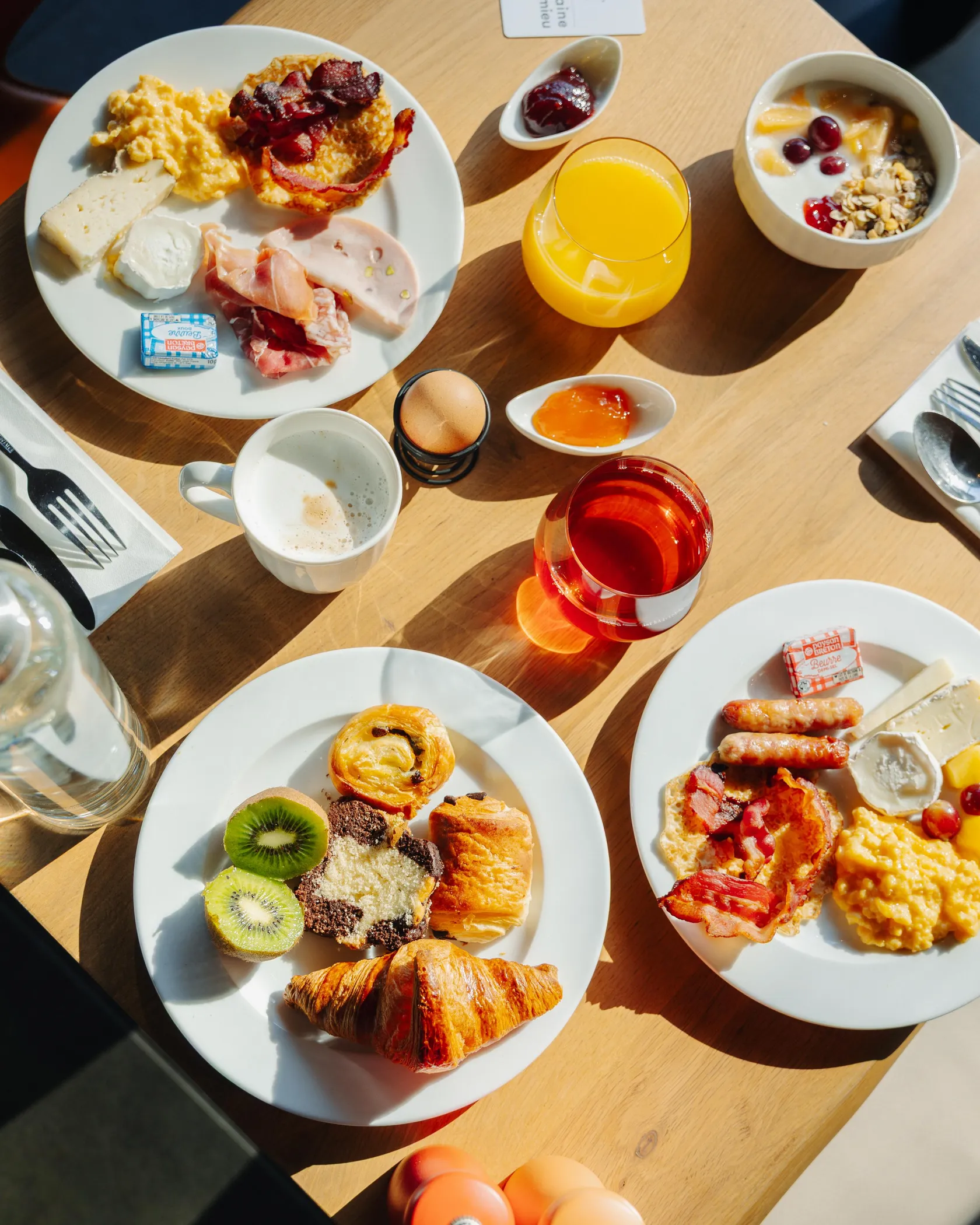 Eine Mahlzeit bestehend aus verschiedenen Gerichten, darunter Eier, Fleisch, Käse, Obst, Gebäck, Getränke und Gewürze, auf einem Holztisch angerichtet