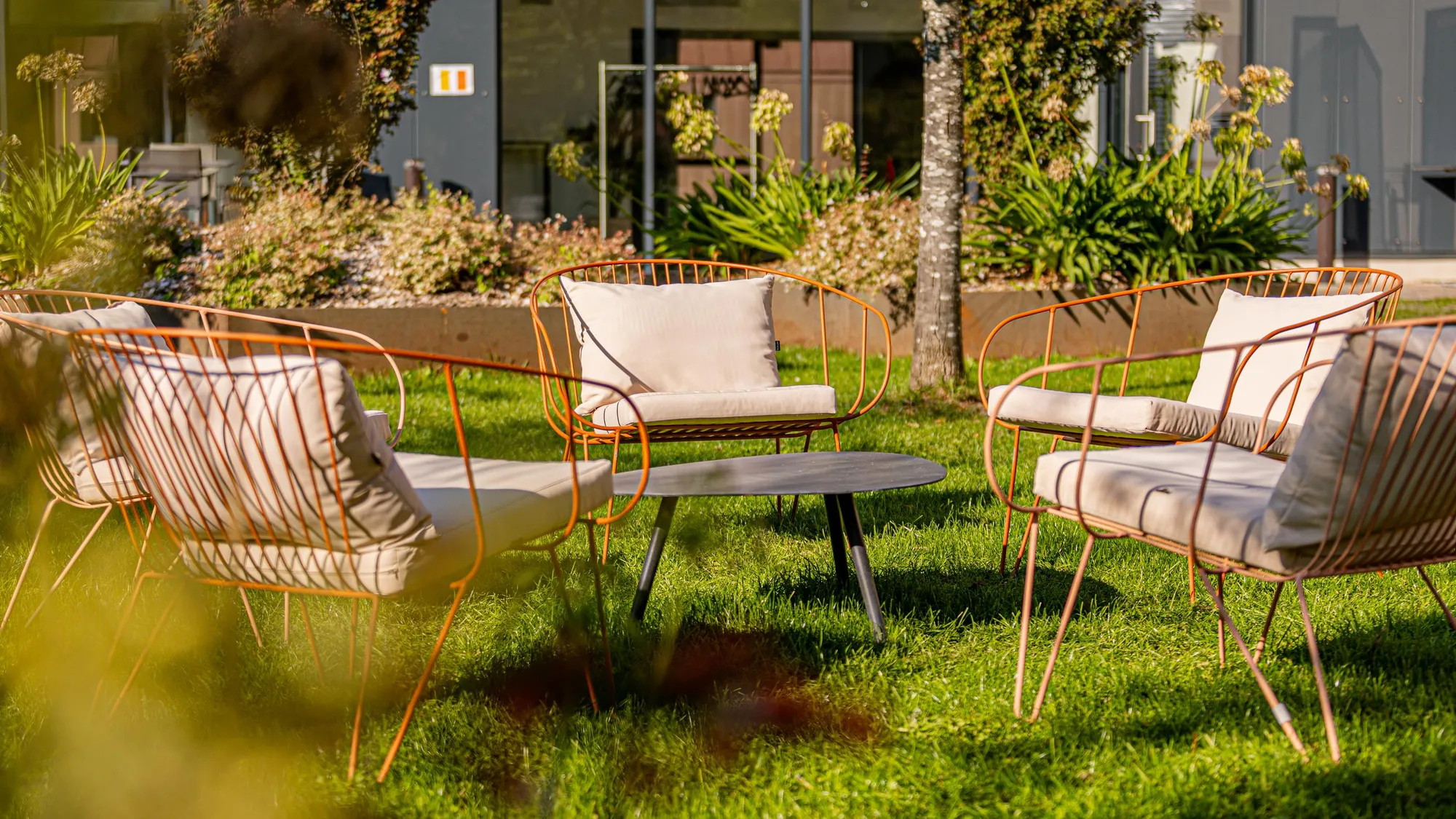 Quatre fauteuils en métal orange avec des coussins beiges autour d'une petite table noire sur une pelouse verte