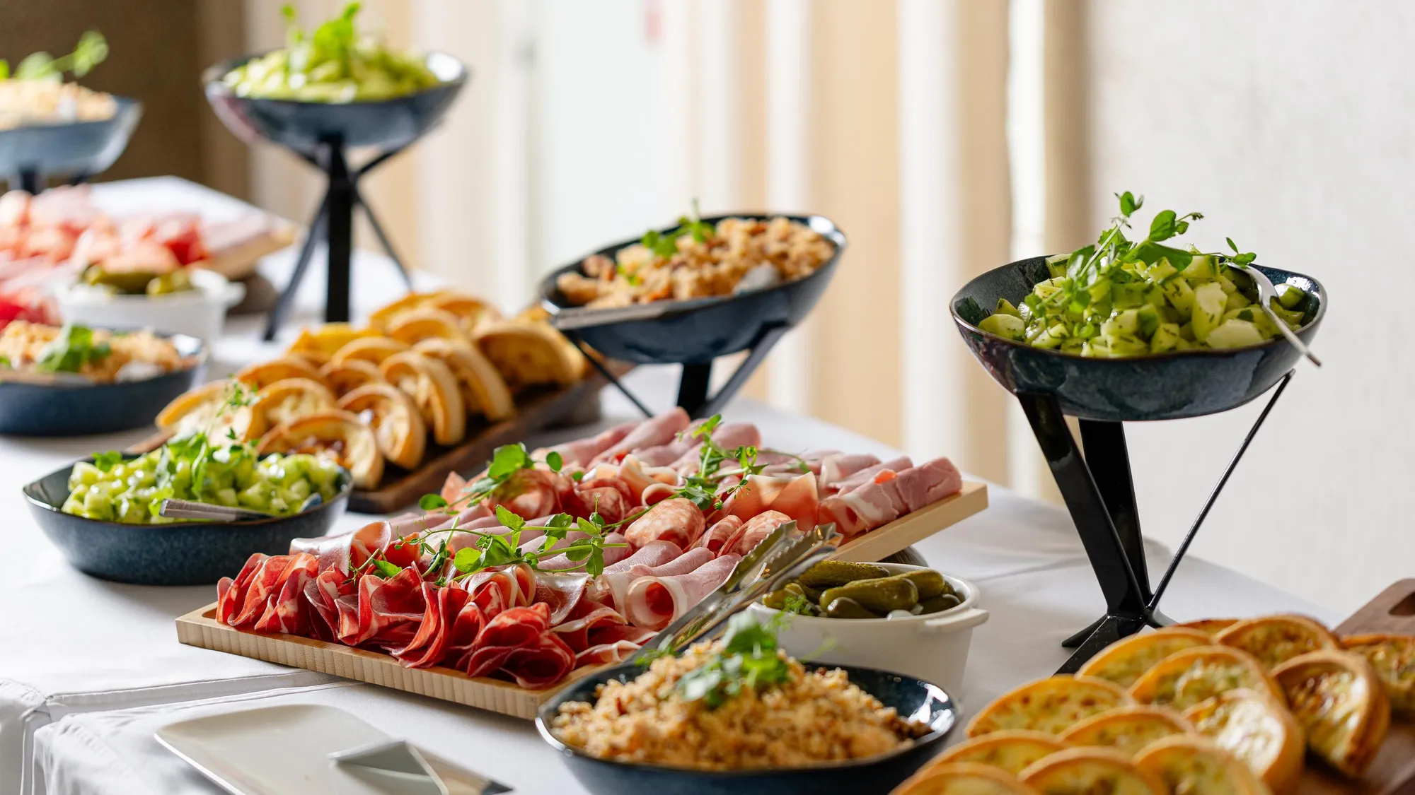 Un assortiment de plats froids incluant des charcuteries, des salades, des olives et du pain est présenté sur une table