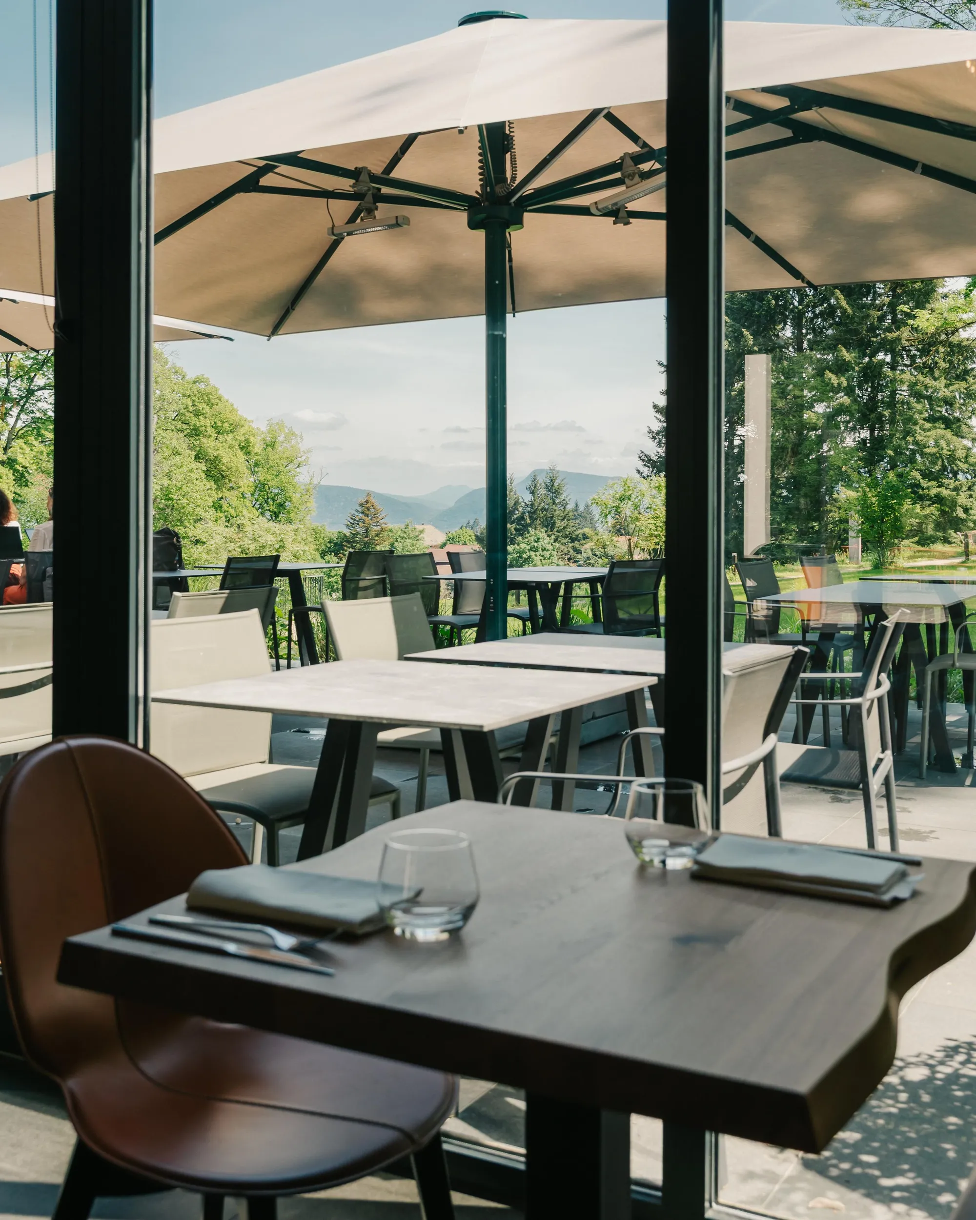 Tisch mit Besteck, Gläsern und Servietten gedeckt in einem Restaurant mit Terrasse und Blick auf Berge und Bäume
