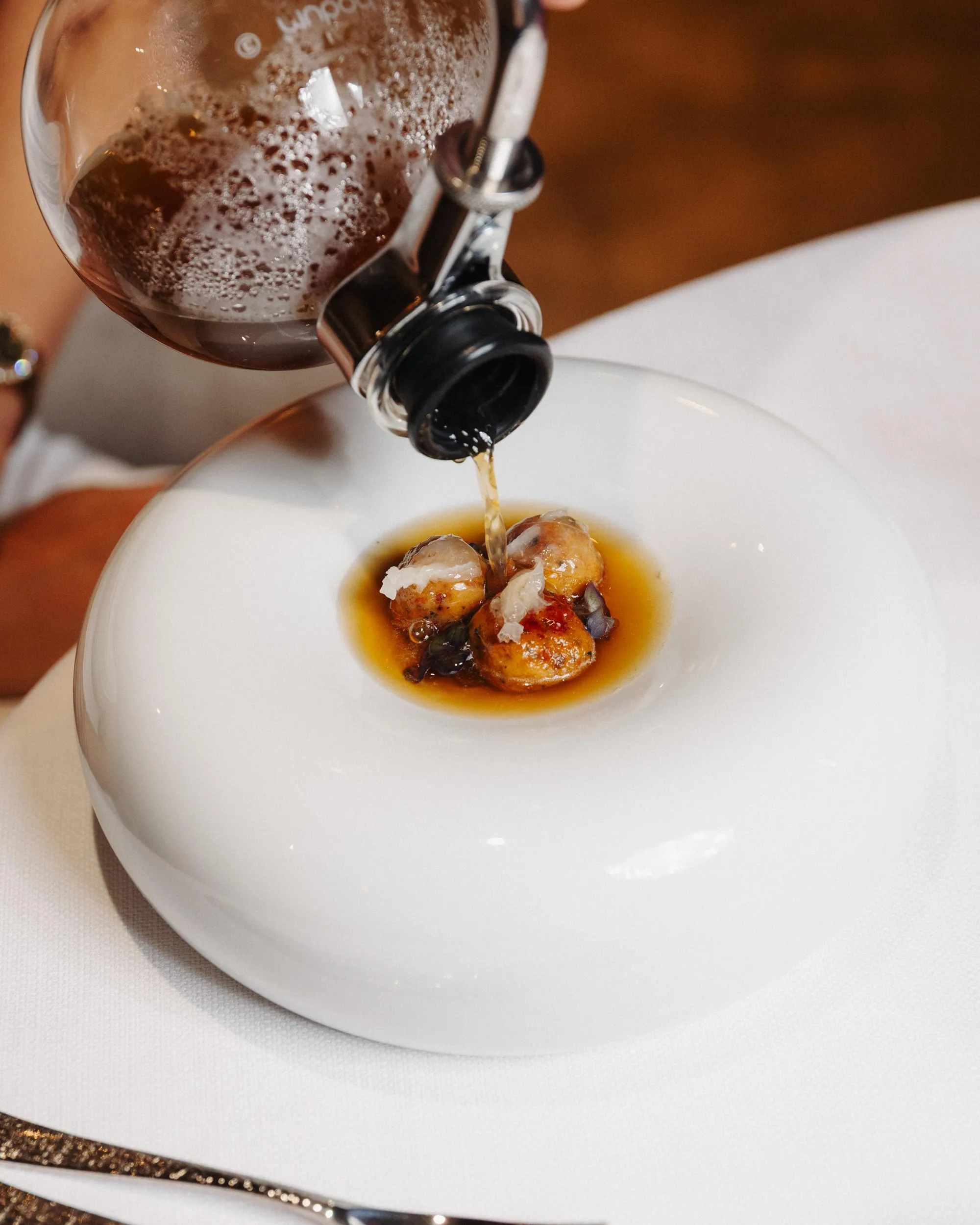Un liquide est versé sur une petite portion de nourriture dans une assiette blanche