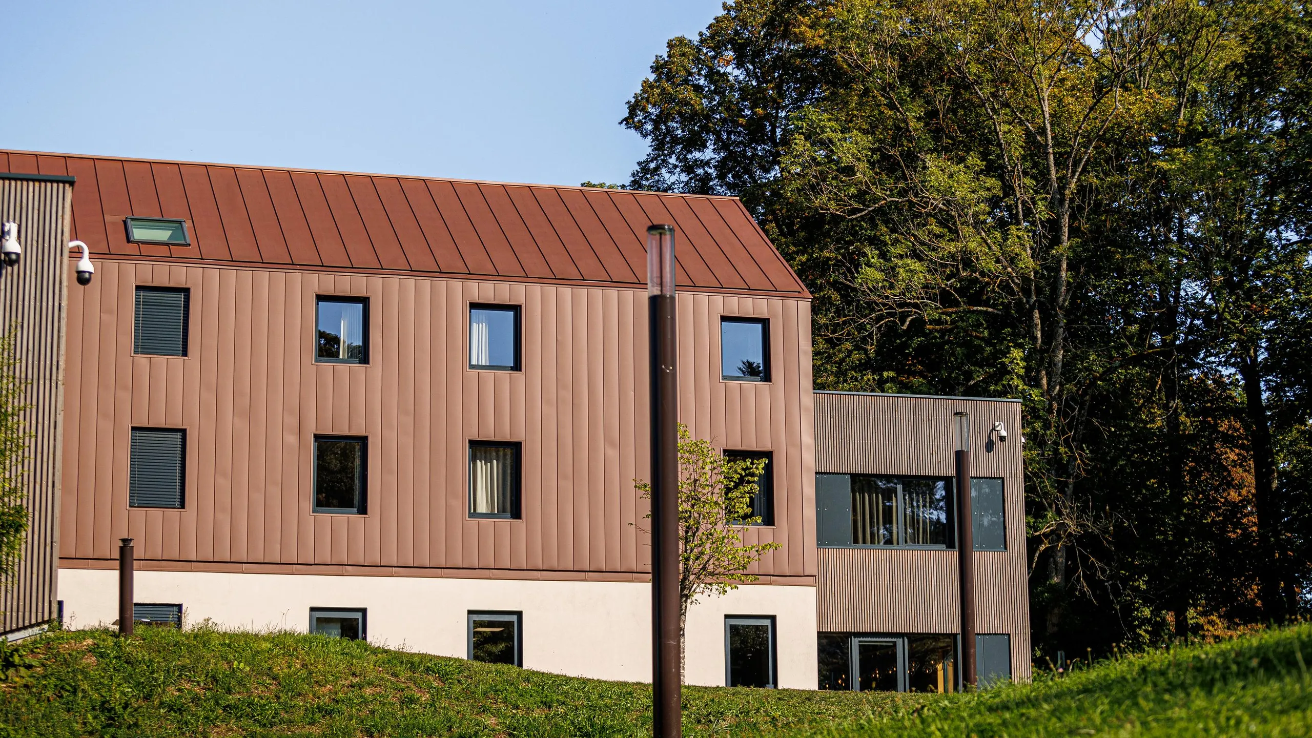 Maison moderne en bois avec façade marron et toiture rouge, située dans un environnement verdoyant