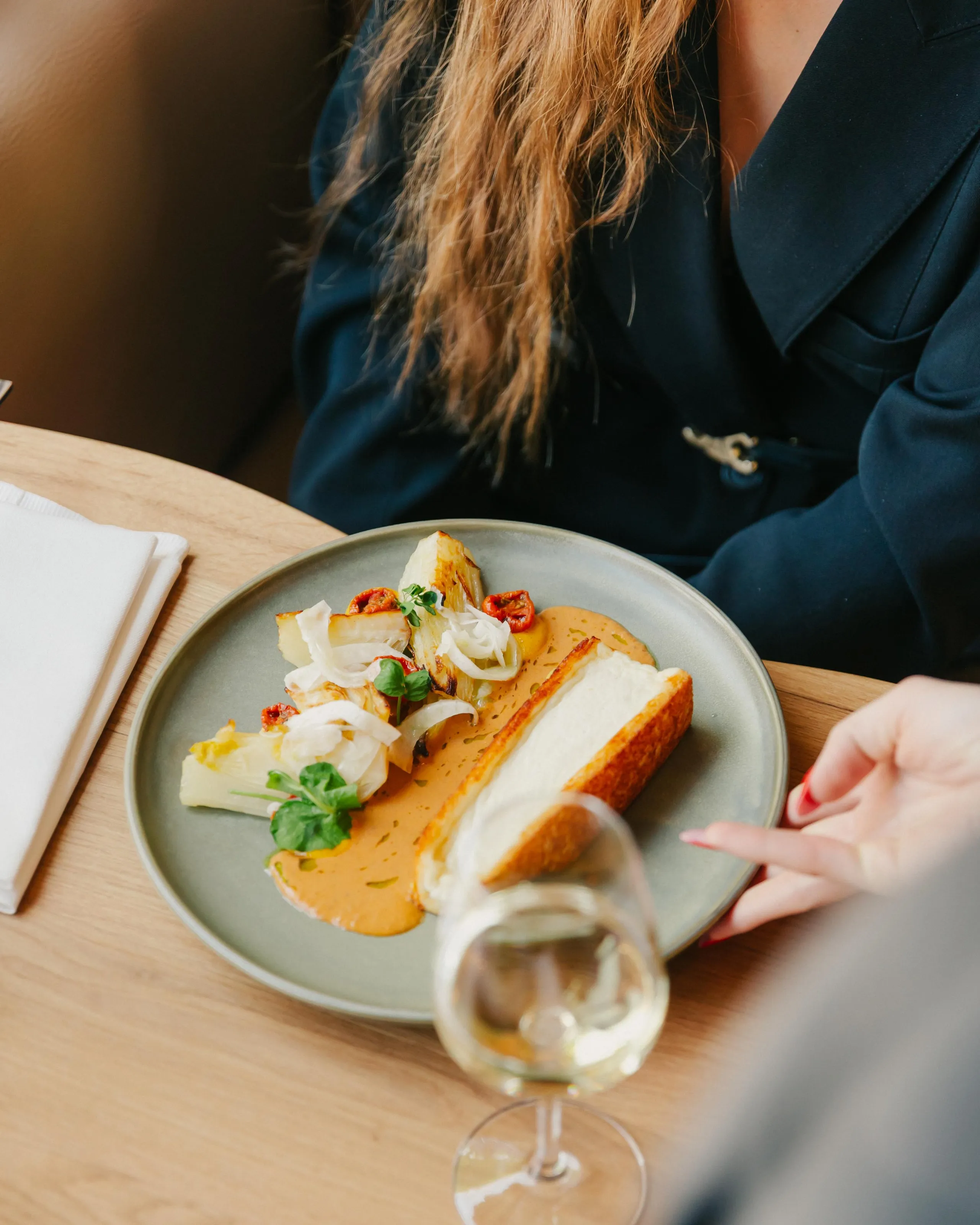 Eine Person isst ein mit Käse, Zwiebeln und Chili belegtes Toastbrot und trinkt dazu ein Glas Weißwein.