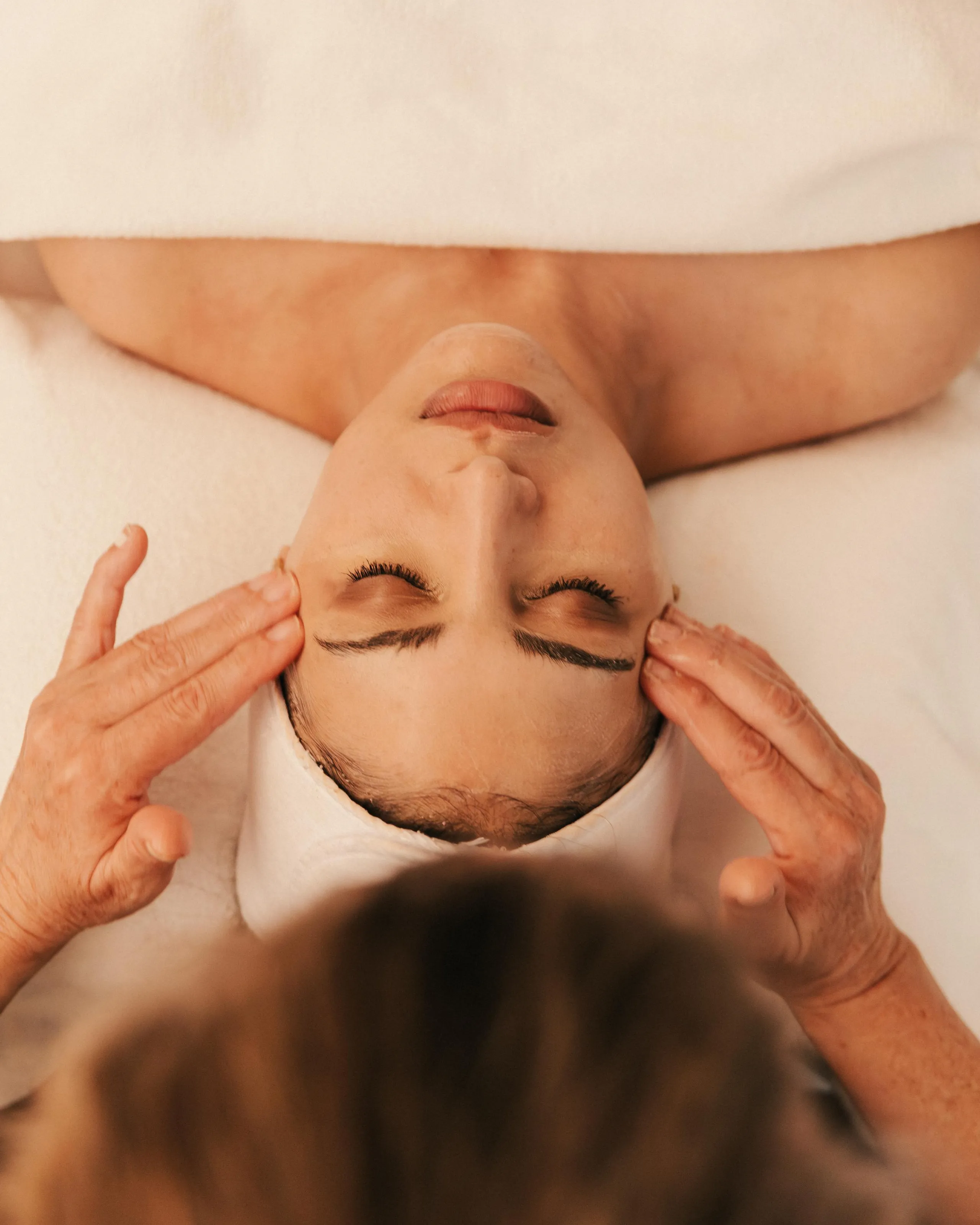 Une personne allongée sur le dos reçoit un massage des tempes par des mains expertes