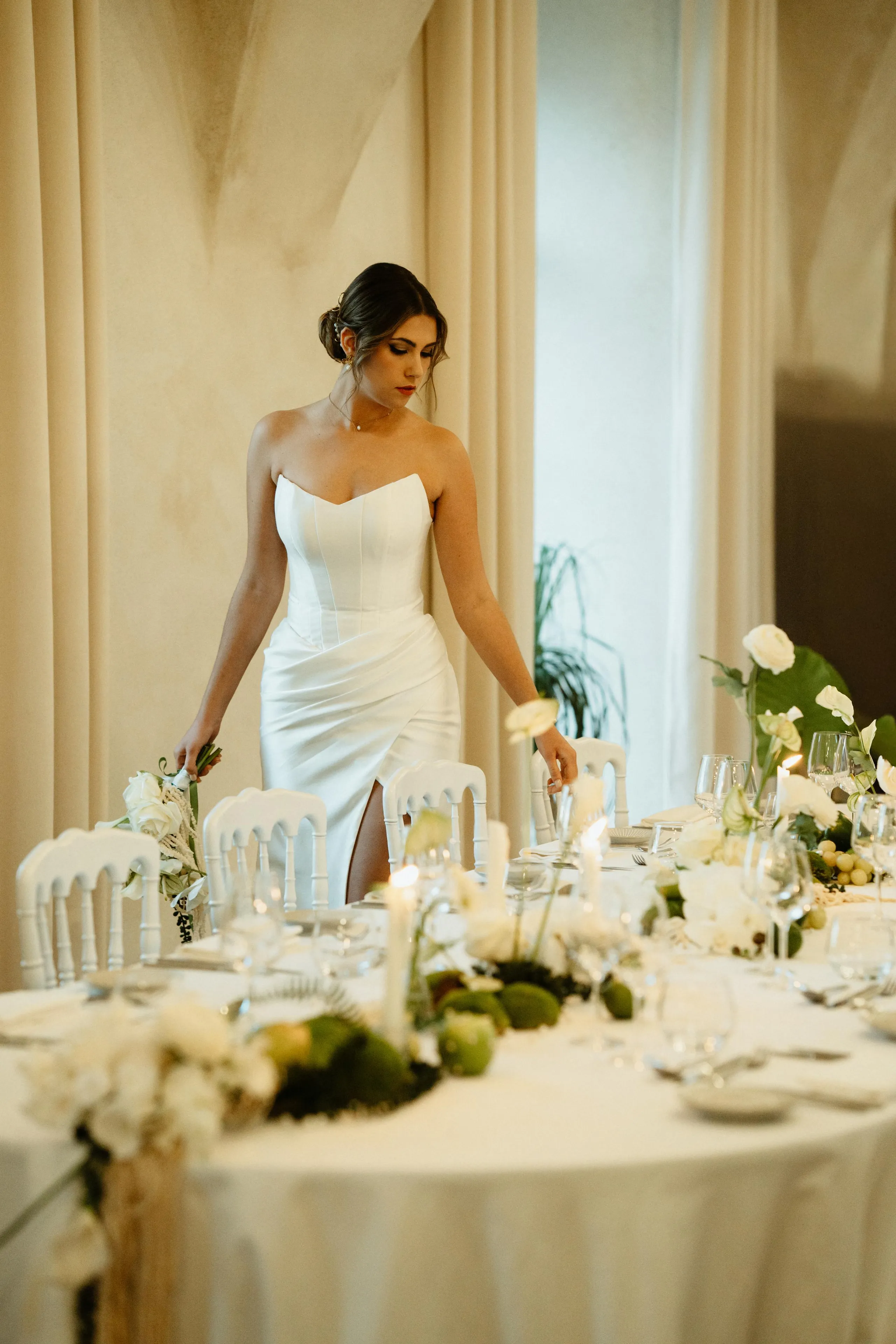 Une femme en robe de mariée blanche se tient près d'une table de réception décorée de fleurs et de verres à vin