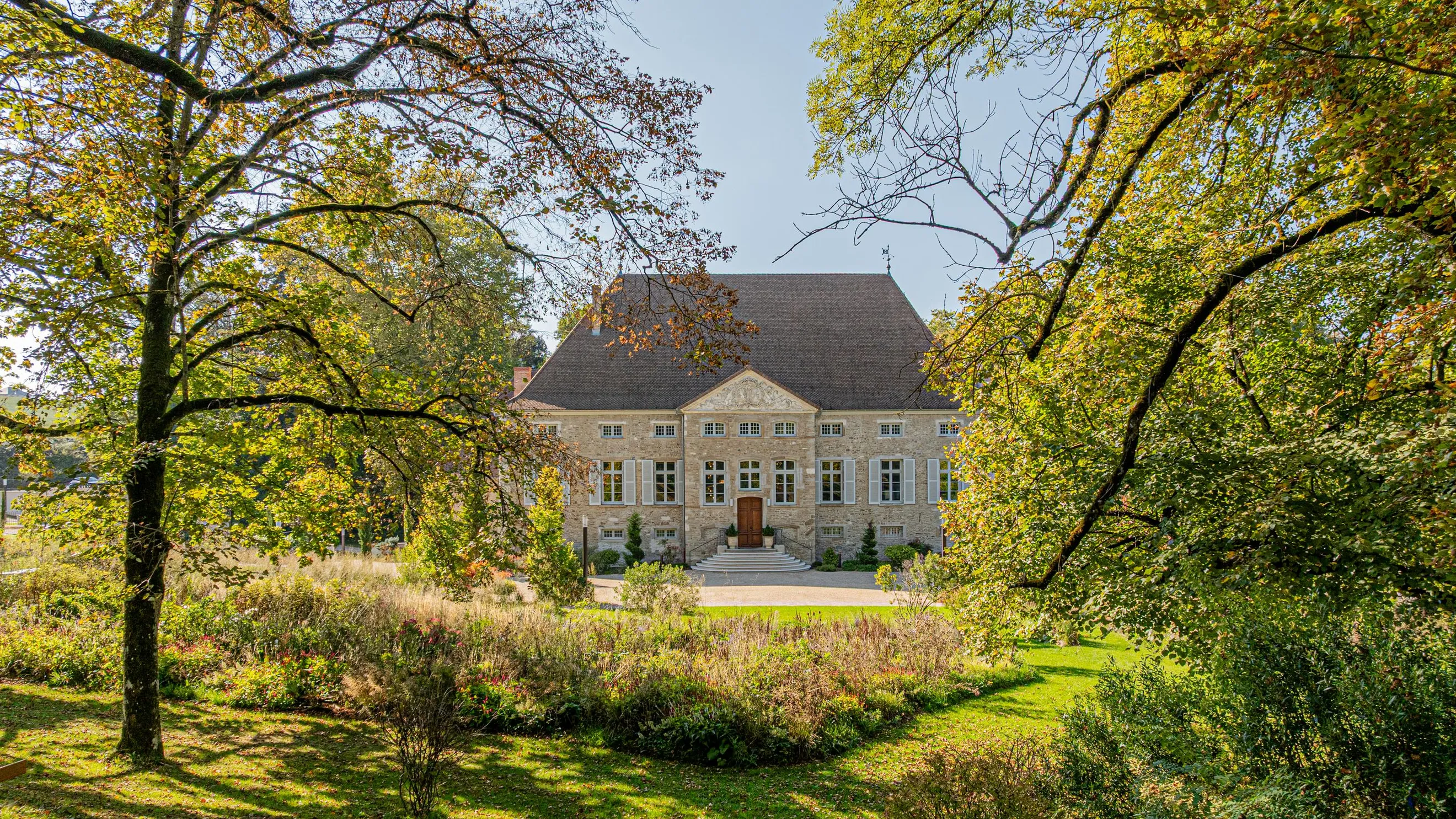 Maison en pierre avec toit en ardoise entourée d'arbres et de végétation en automne