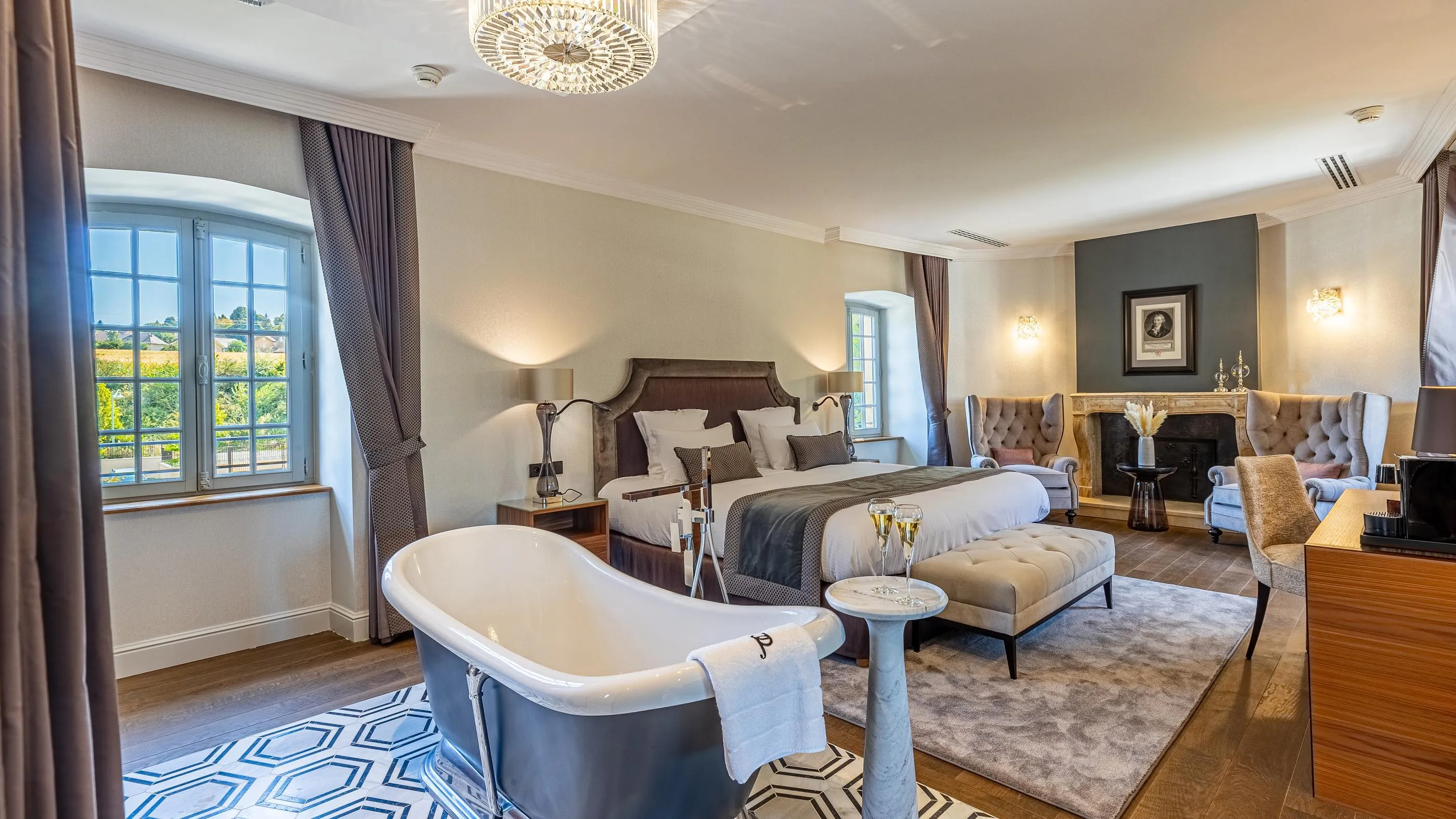 Chambre luxueuse avec lit double, baignoire indépendante, cheminée, fenêtres panoramiques et mobilier élégant