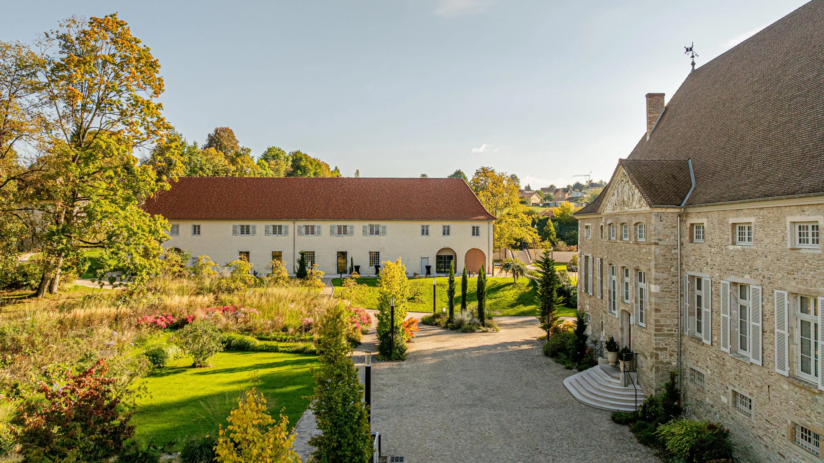 Old stone farmhouse with a flower garden and buildings with red-tiled roofs under a clear sky