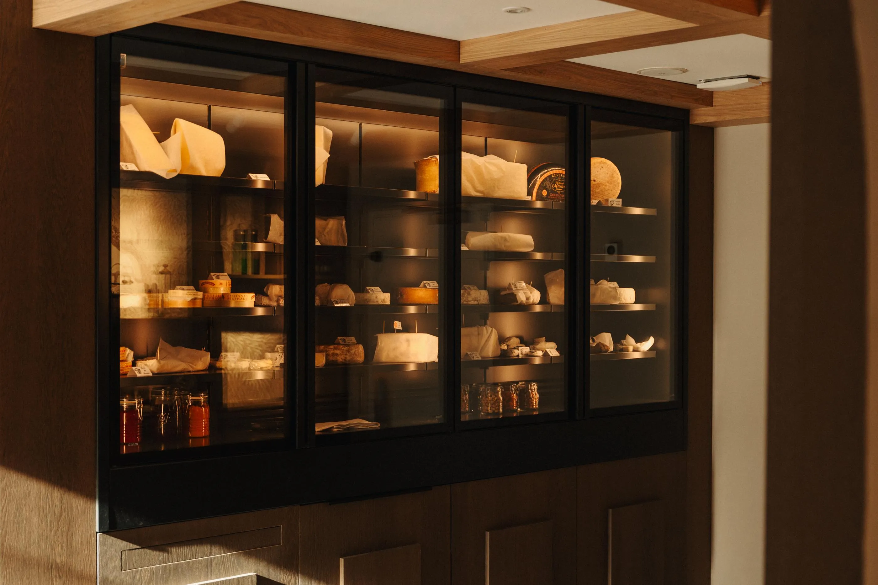 Une vitrine en verre noir expose divers fromages et condiments sur des étagères éclairées