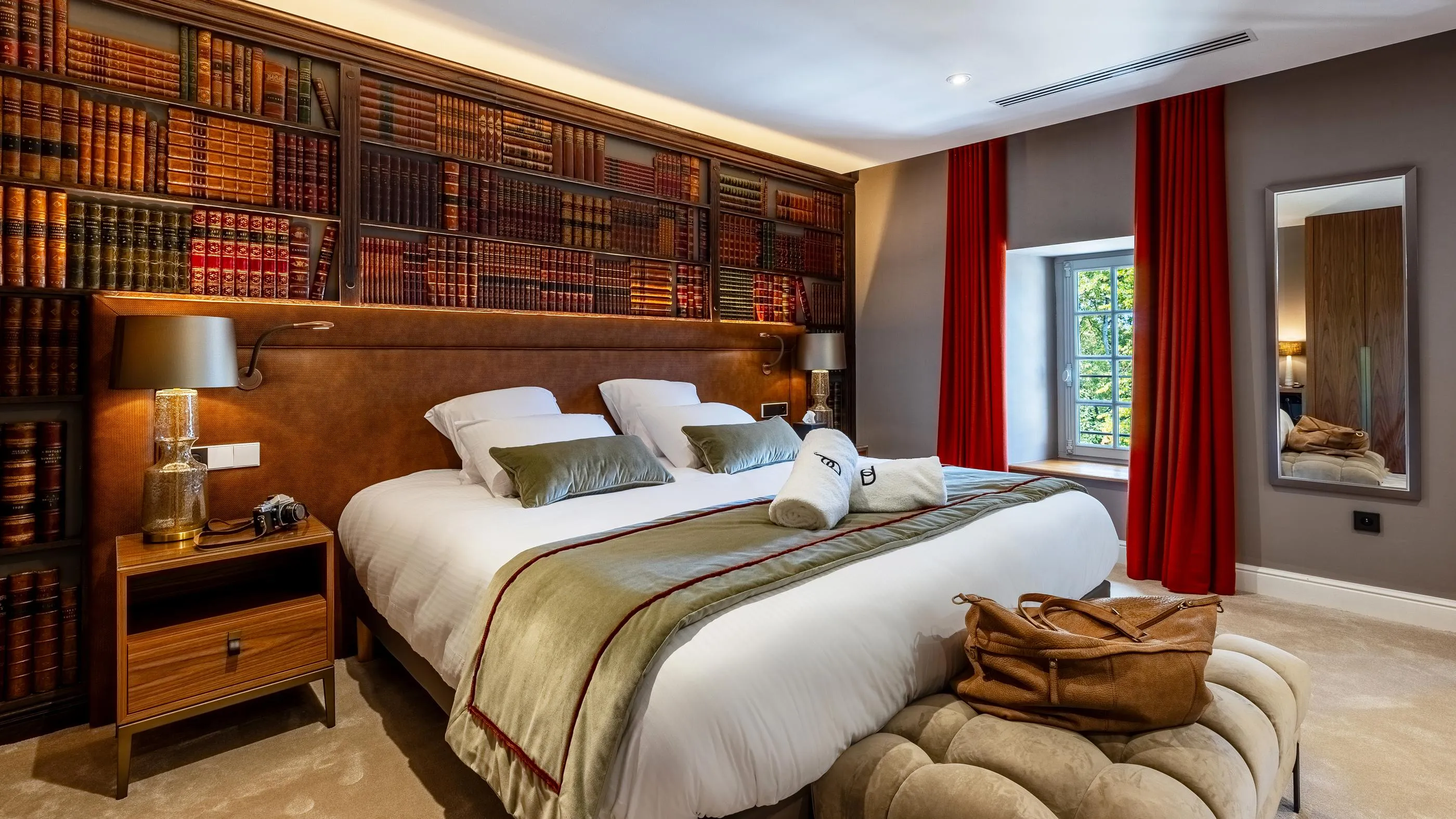 Elegante Zimmer mit einem Doppelbett, Bücherregalen, Nachttischlampen und einem Fenster mit roten Vorhängen