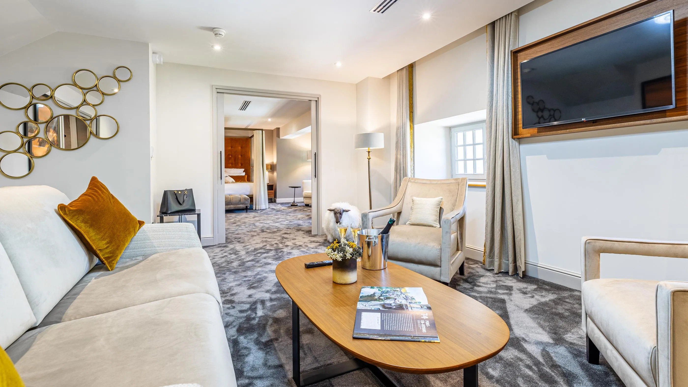 Hotel lounge with sofa, armchairs, coffee table, lamps and view of the bedroom