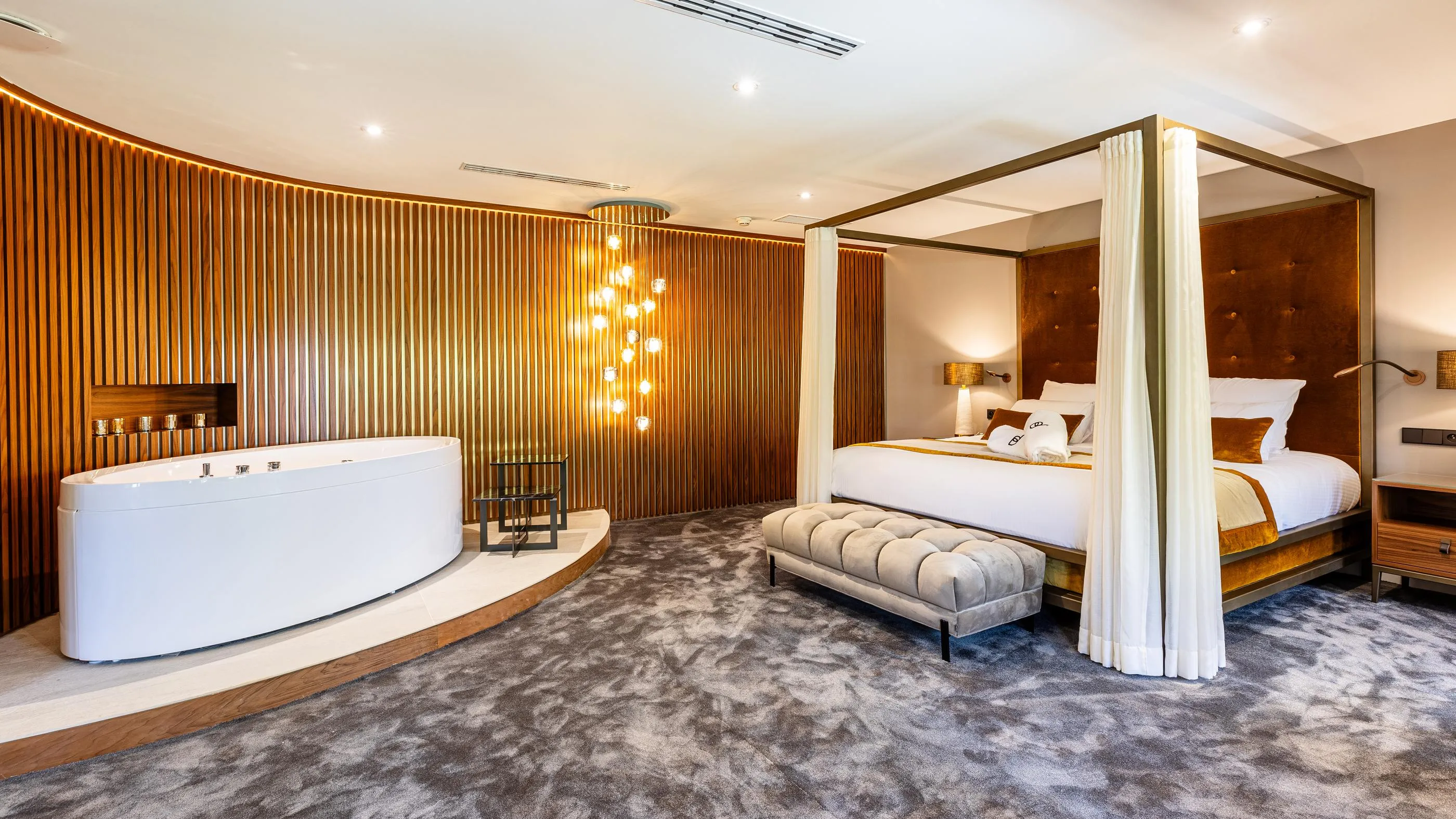 Chambre luxueuse avec un lit à baldaquin, une baignoire encastrée et un mur décoré de lattes en bois éclairées
