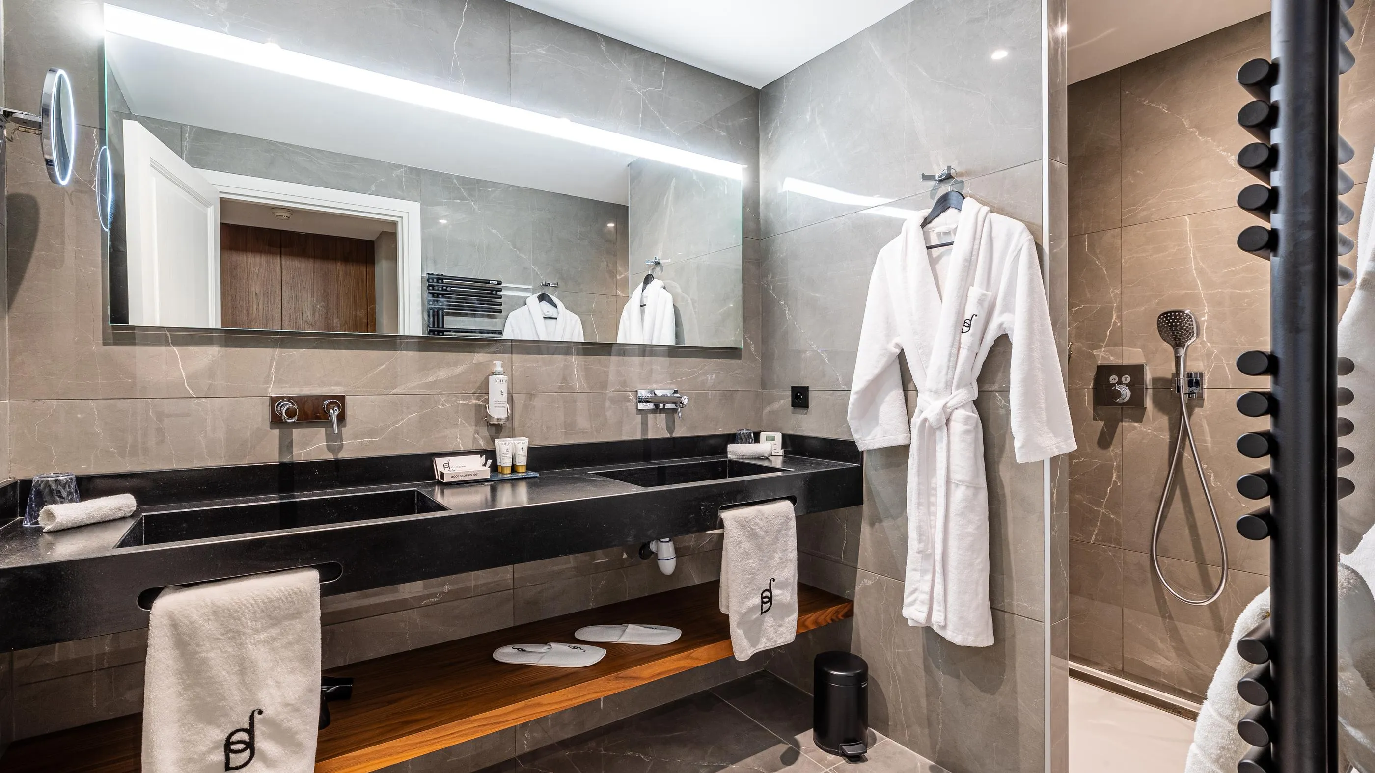 Modern bathroom with double sink, mirror, white robes, and Italian shower