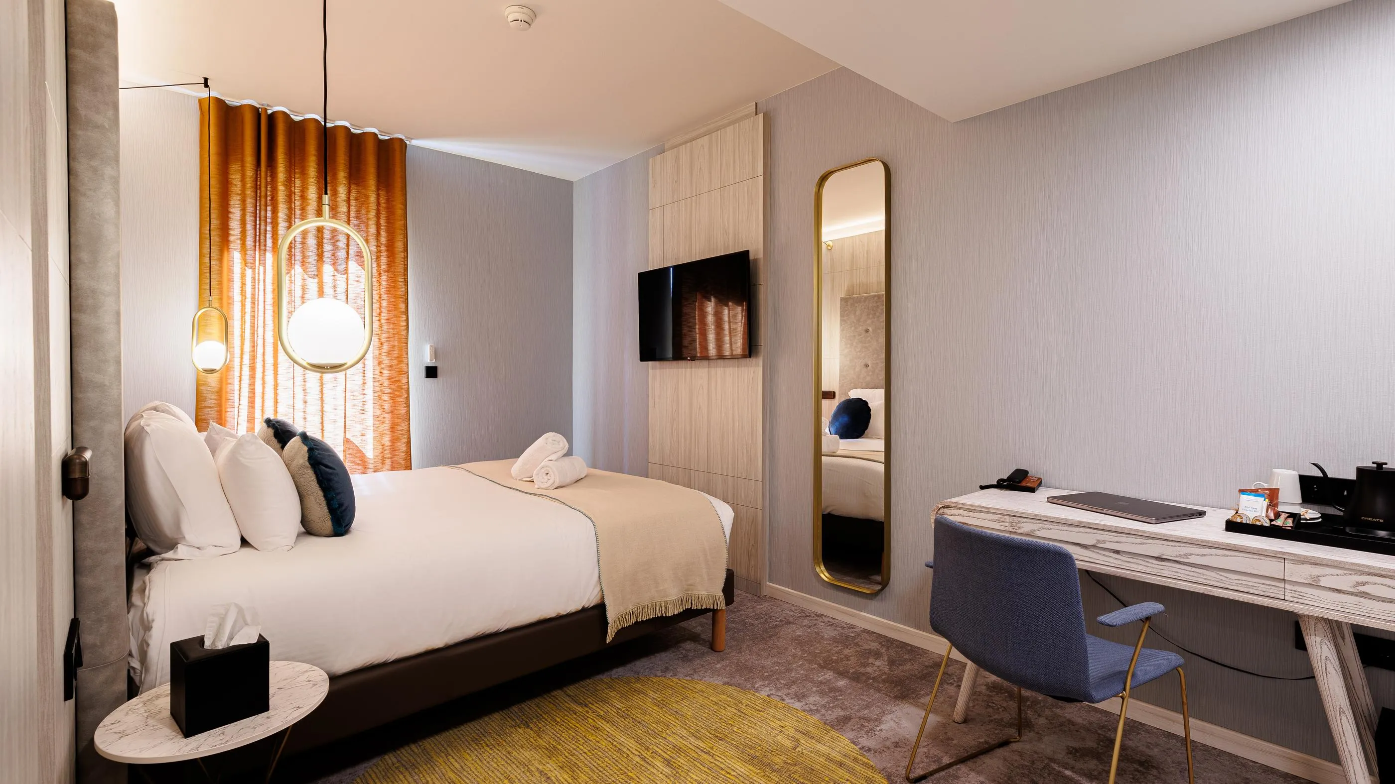 Hotelzimmer mit einem Einzelbett, einem Schreibtisch, einem Wandfernseher und hängenden Lampen
