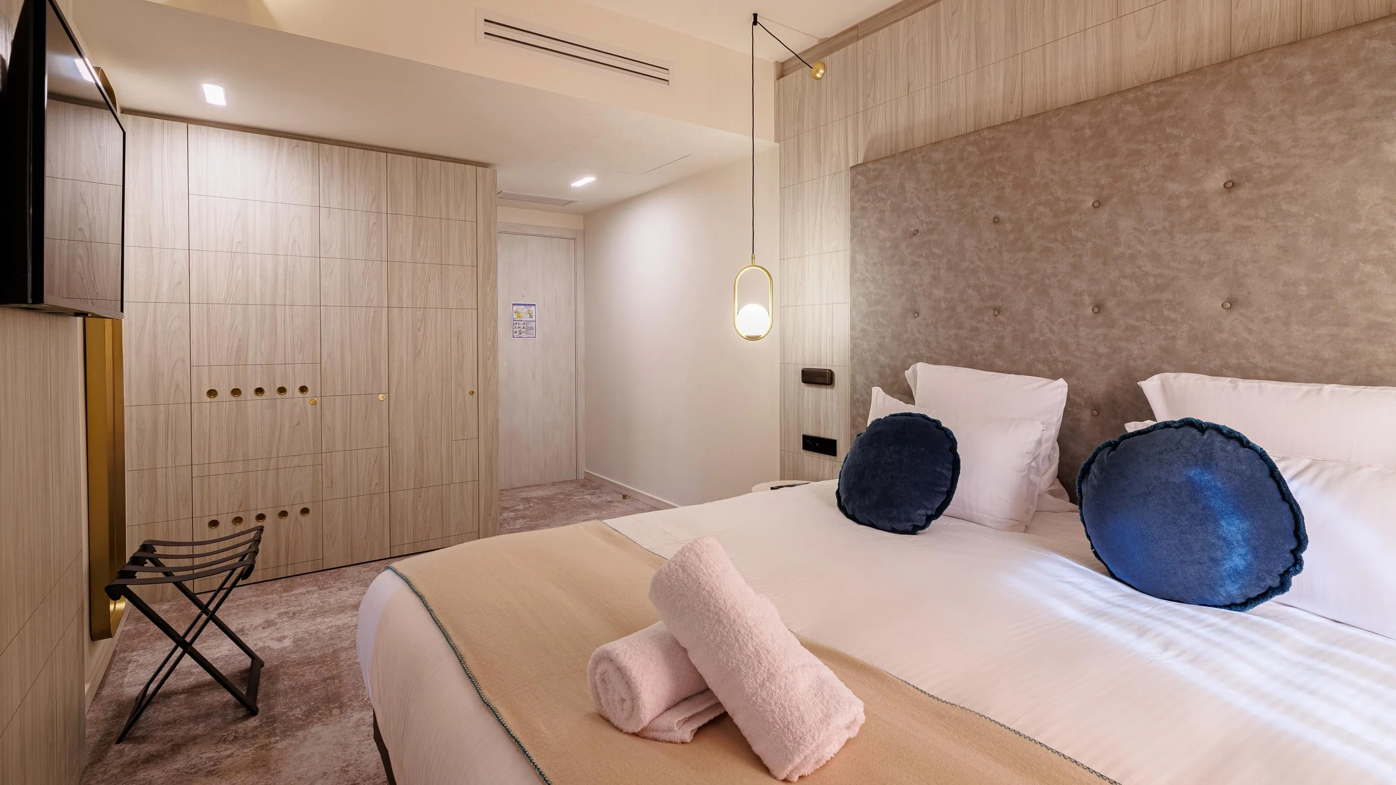 Chambre d'hôtel moderne avec un lit double, des coussins, des serviettes roulées et un éclairage mural