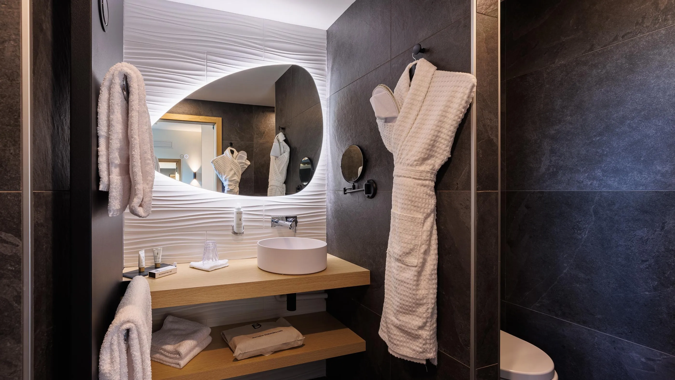 Moderne Badezimmer mit Waschbecken, Spiegel, Handtüchern und Toilettenartikeln auf einem Regal