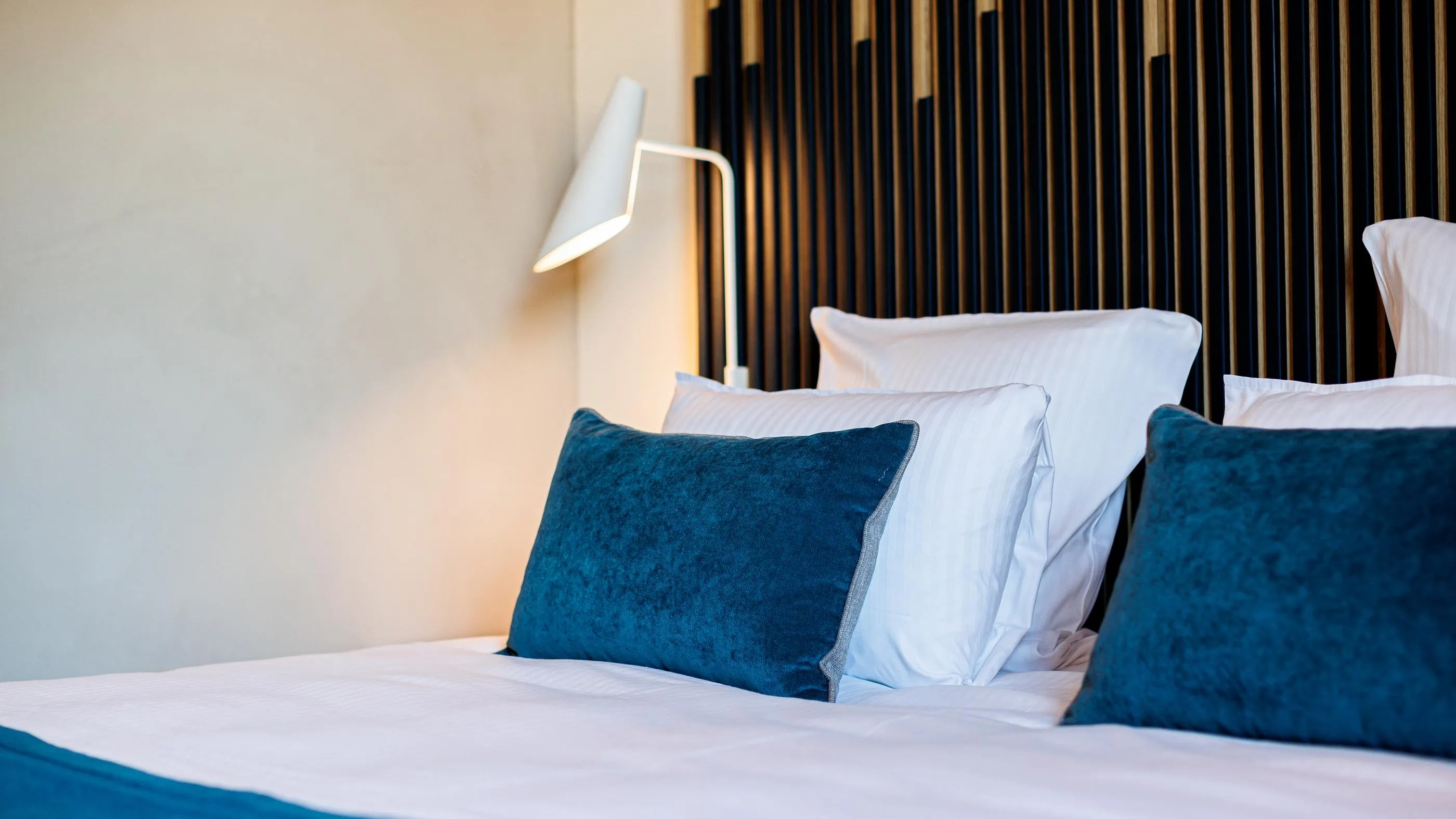 Bed with white and blue cushions, a lit lamp turned on, and a headboard with vertical stripes
