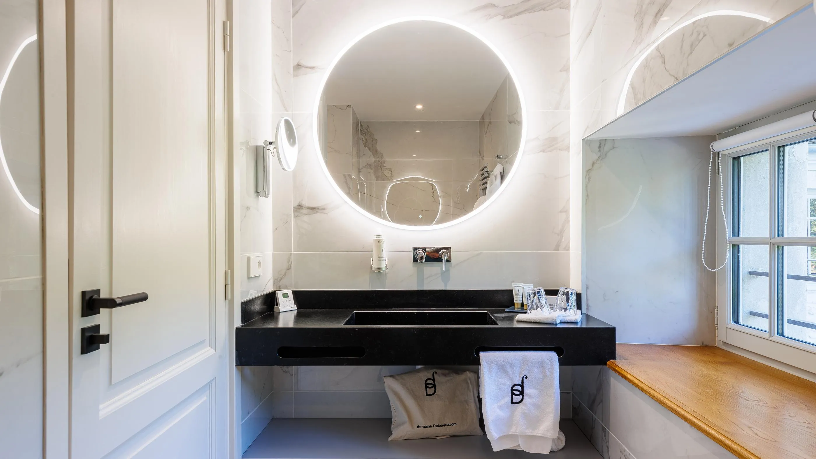 Modern bathroom with double sink, illuminated round mirror and window with blind
