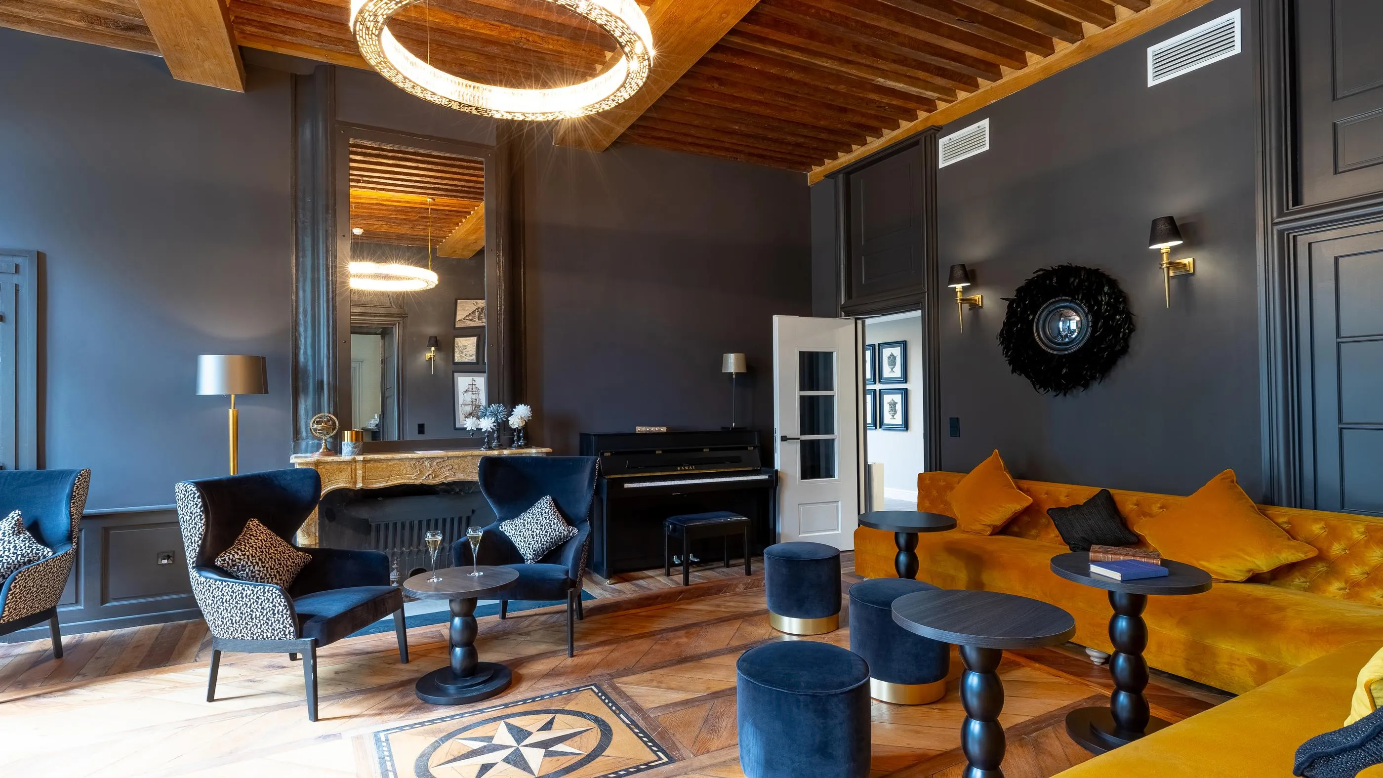 Living room with orange sofa, blue armchairs, and black piano, lit by circular pendant lights