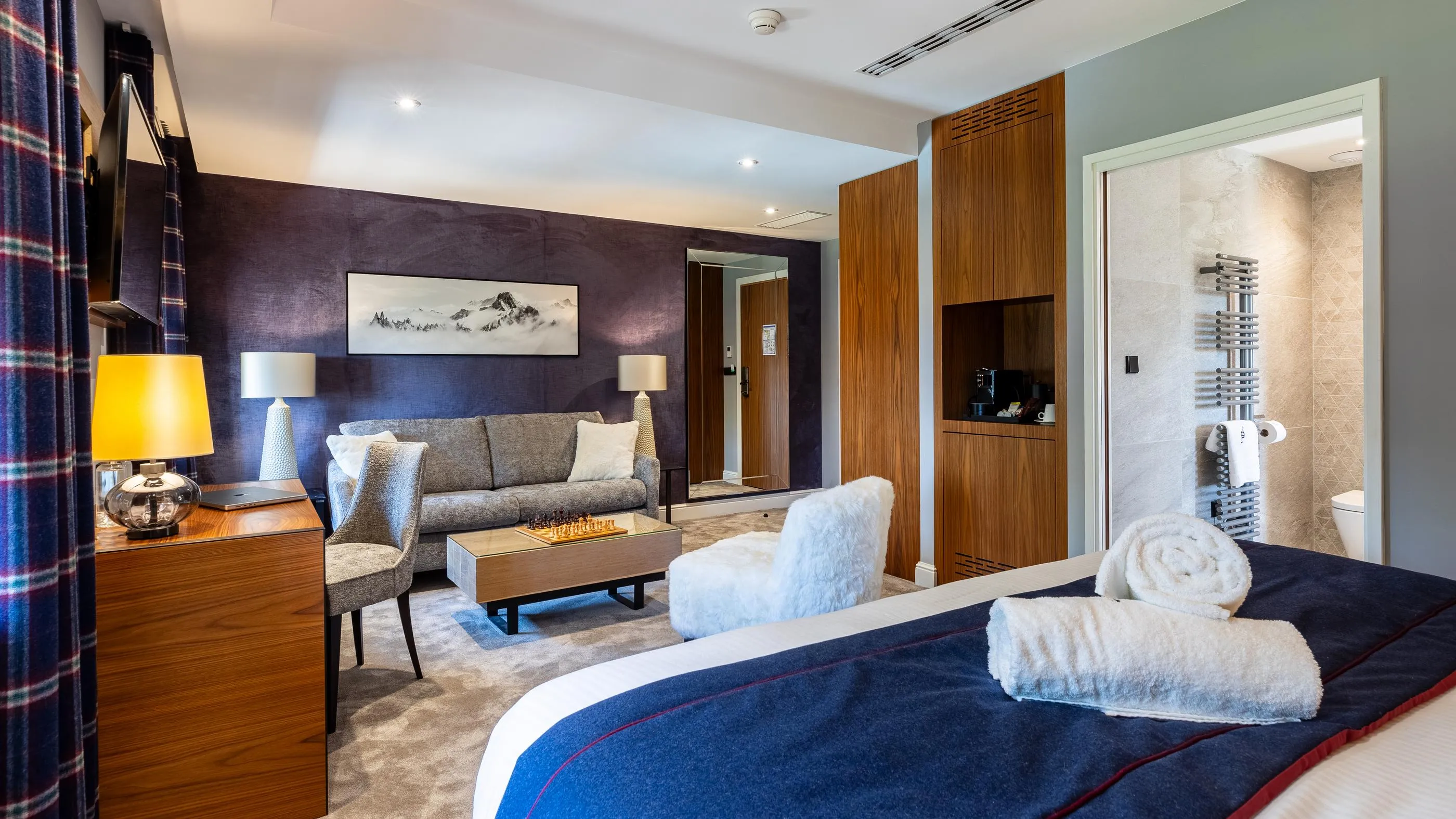 Moderne Hotelzimmer mit Bett, Sofa, Couchtisch, Schreibtisch und im Hintergrund sichtbarer Badezimmer