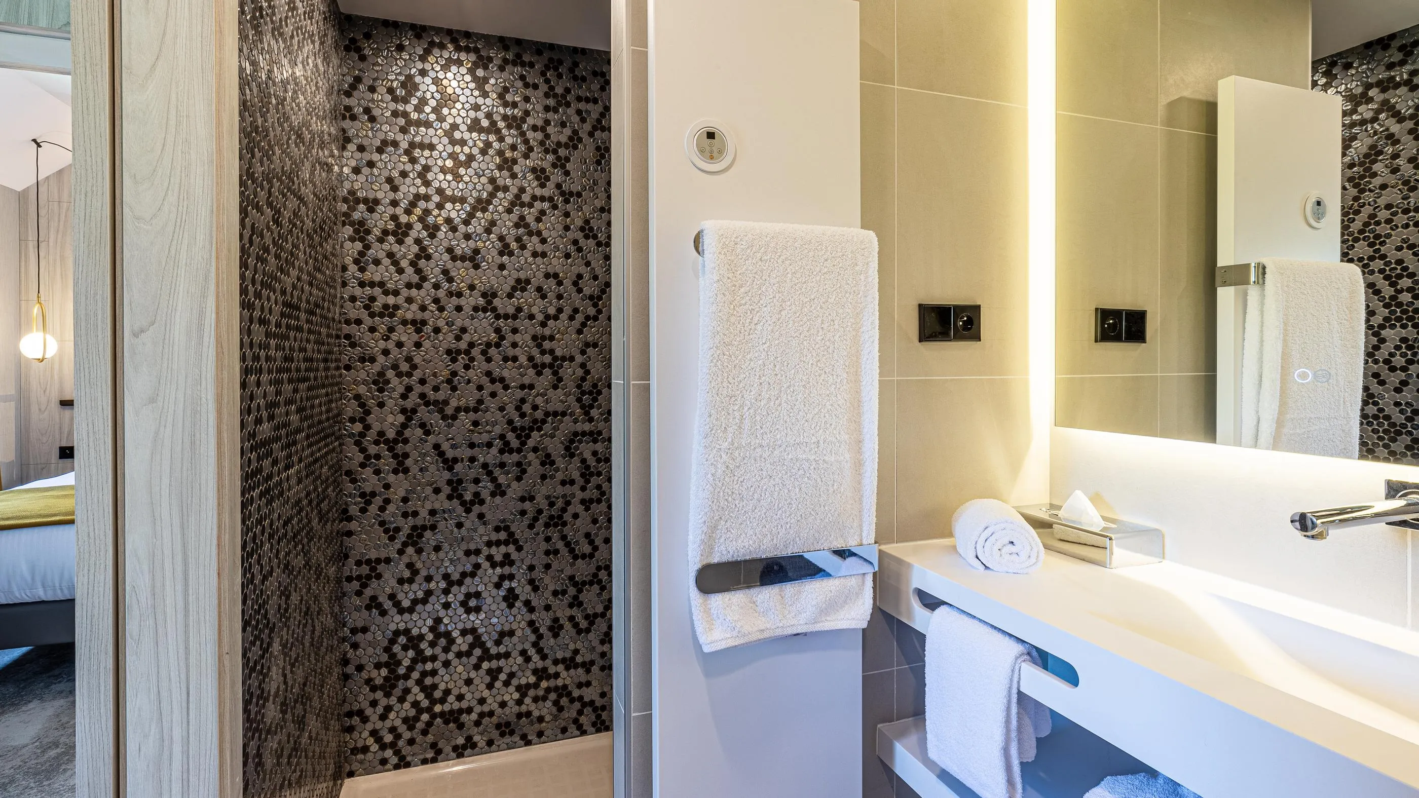 Modernes Badezimmer mit Mosaikdusche, Waschbecken, Handtüchern und Spiegel, der einen Teil des Zimmers reflektiert