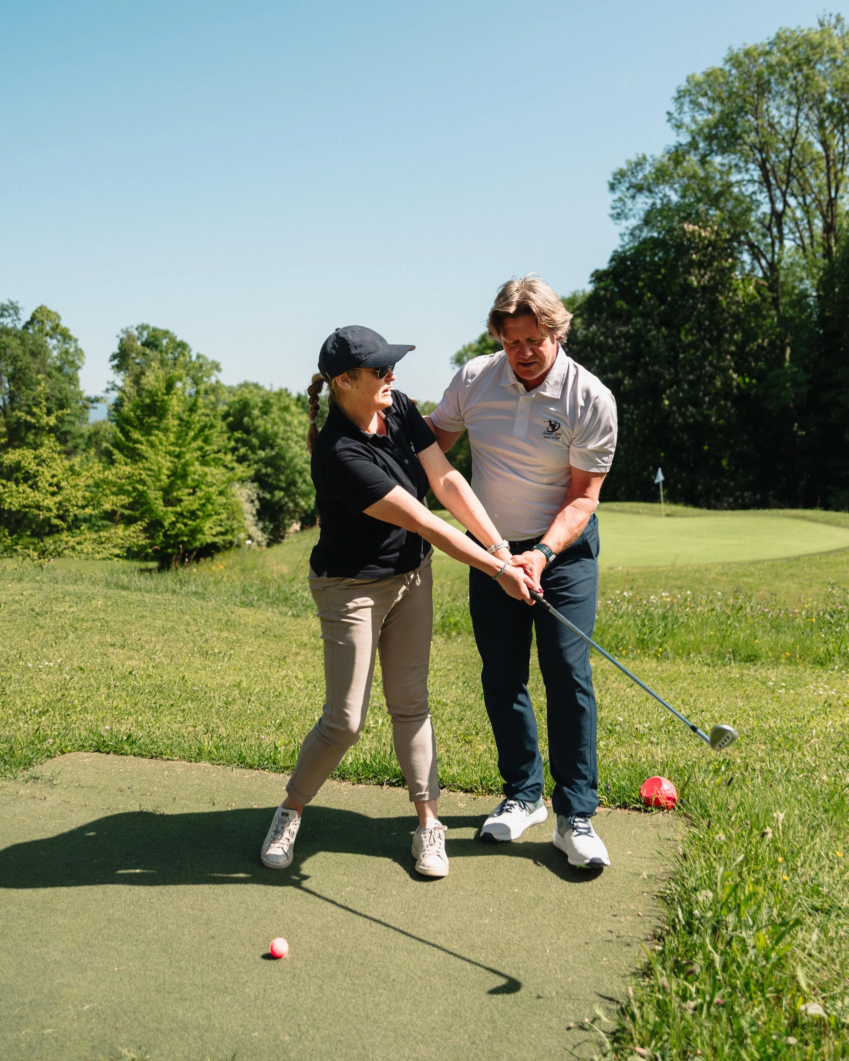 Two people on a golf green, one helping the other adjust their putting stance.