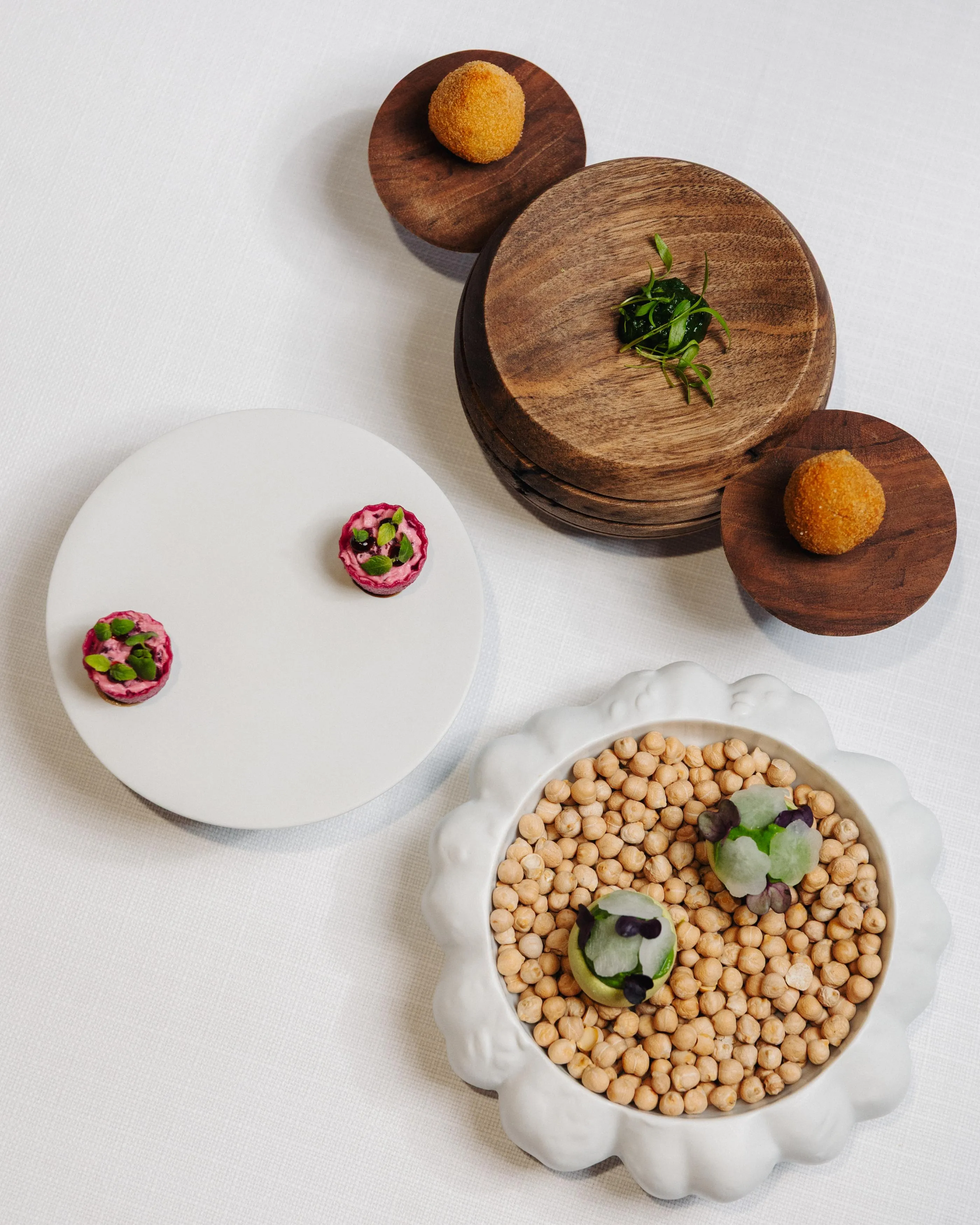 Un plateau avec des plats contenant des boulettes de viande, des légumes et des graines, disposés sur une nappe blanche