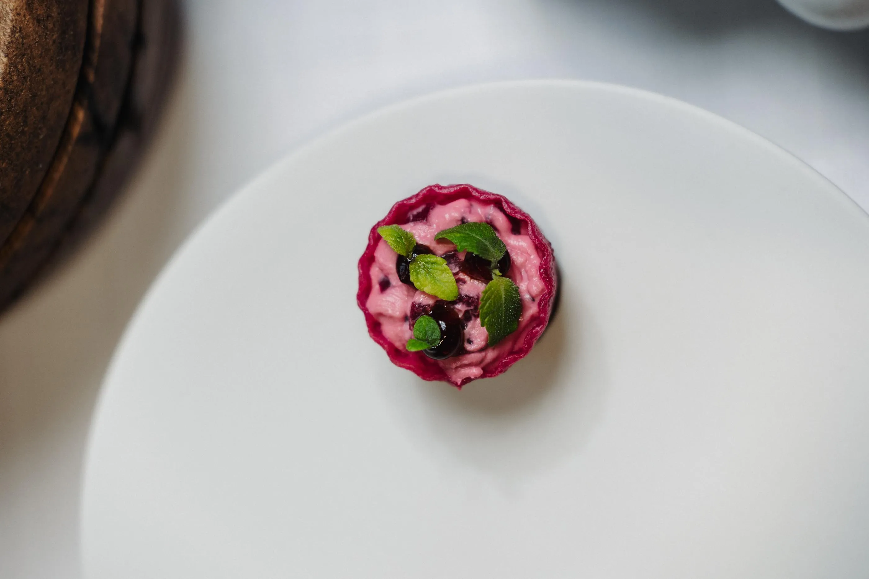 Petite portion de dessert rose garnie de feuilles de menthe et de baies sur une assiette blanche