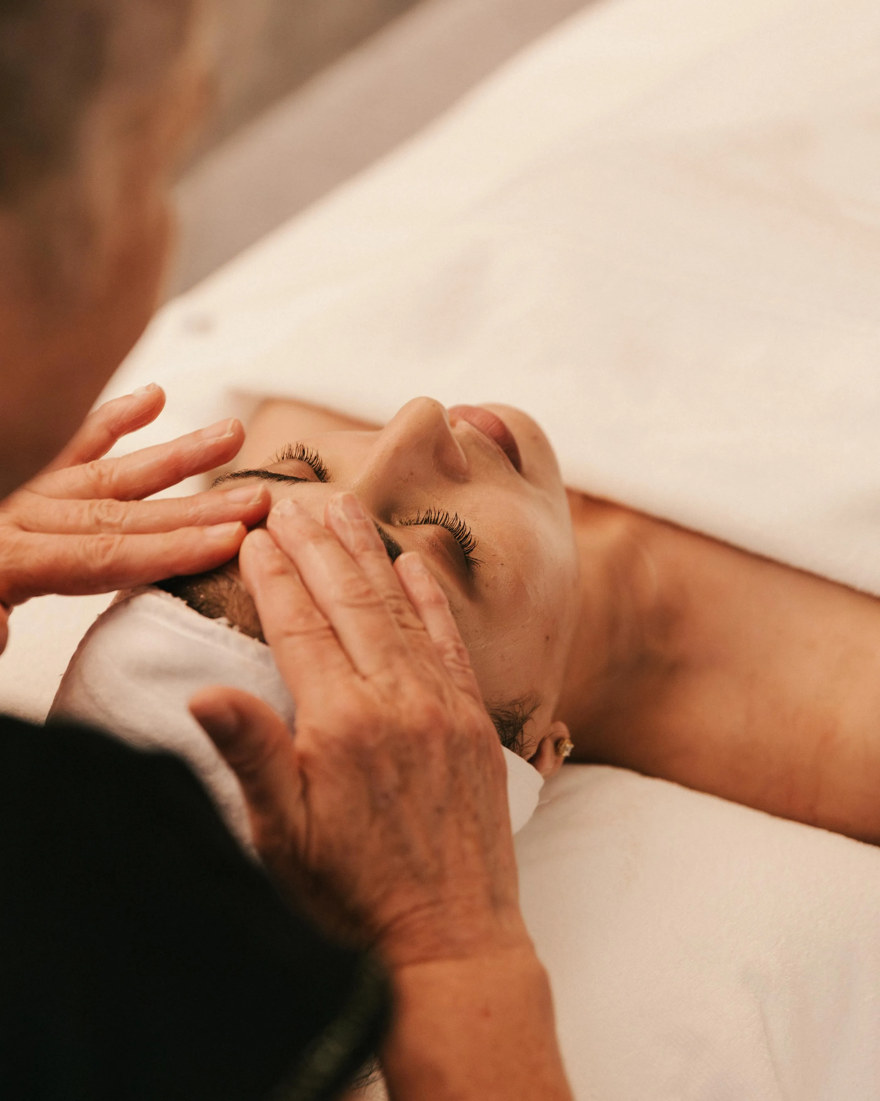 Deux mains massent le visage d'une personne allongée sur le ventre
