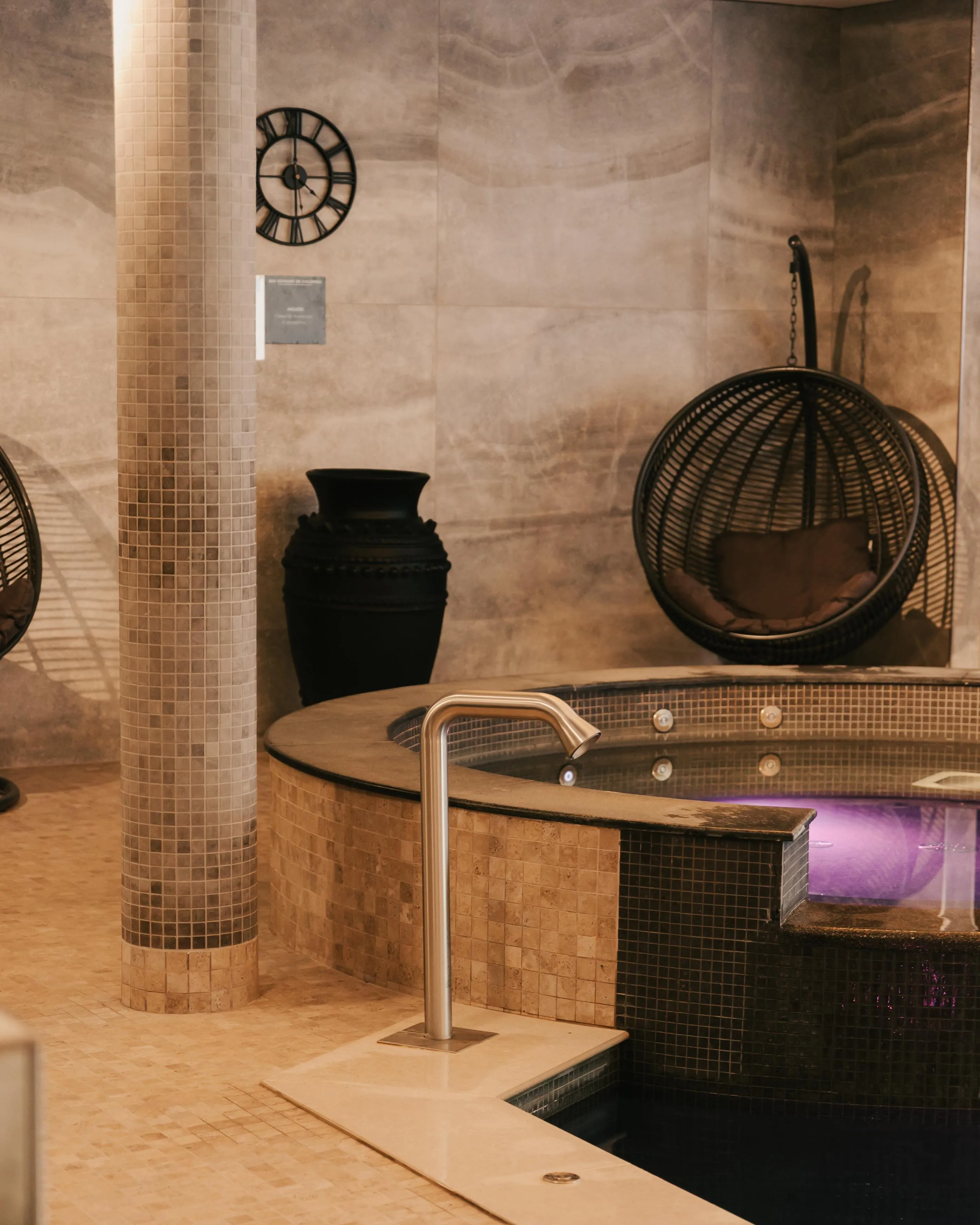 Un lavabo avec robinet et un vase noir sur un comptoir en pierre, avec des miroirs ronds et un mur en carrelage beige