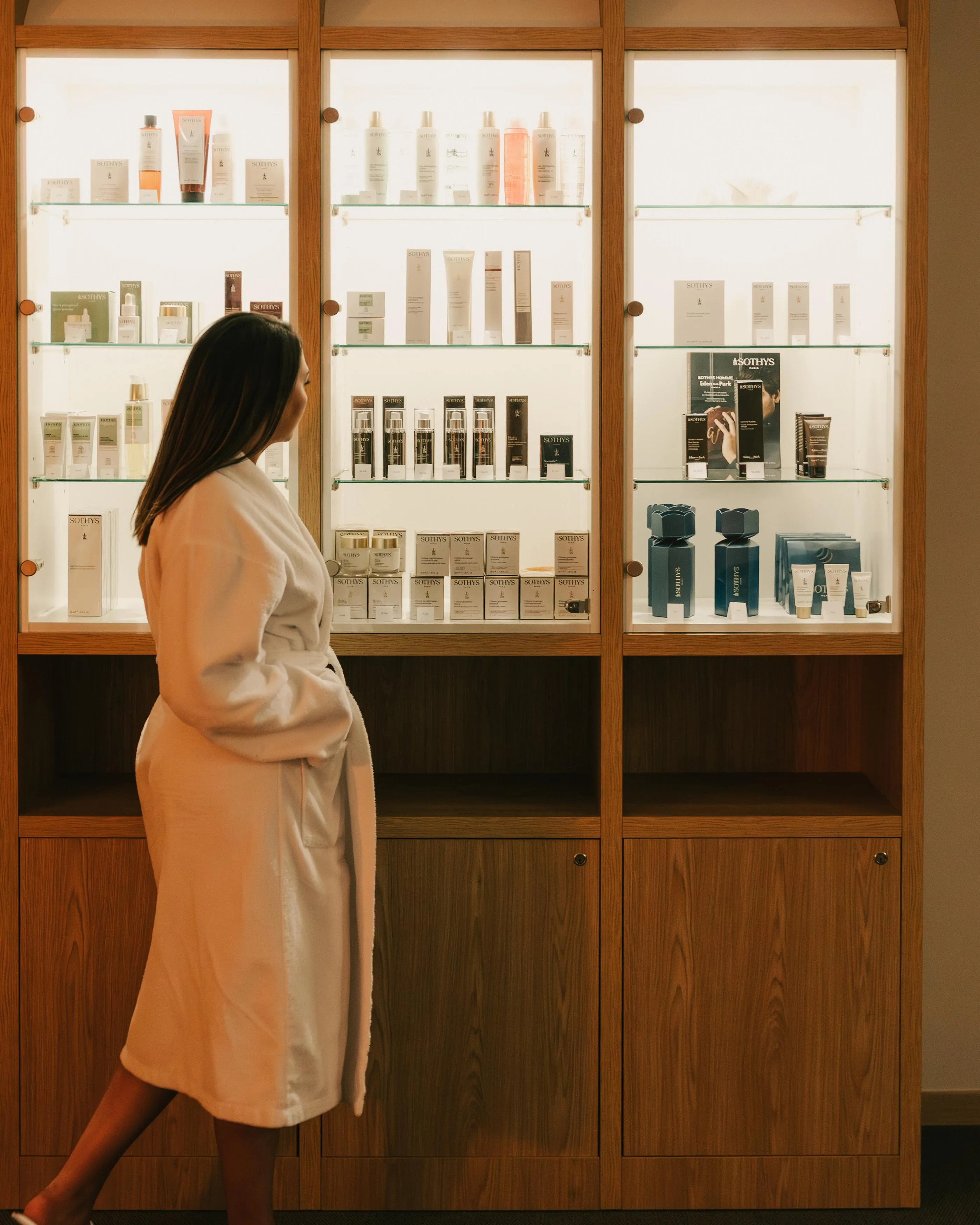 A person in a white swimsuit walks in front of glass shelves filled with Sothys cosmetics.