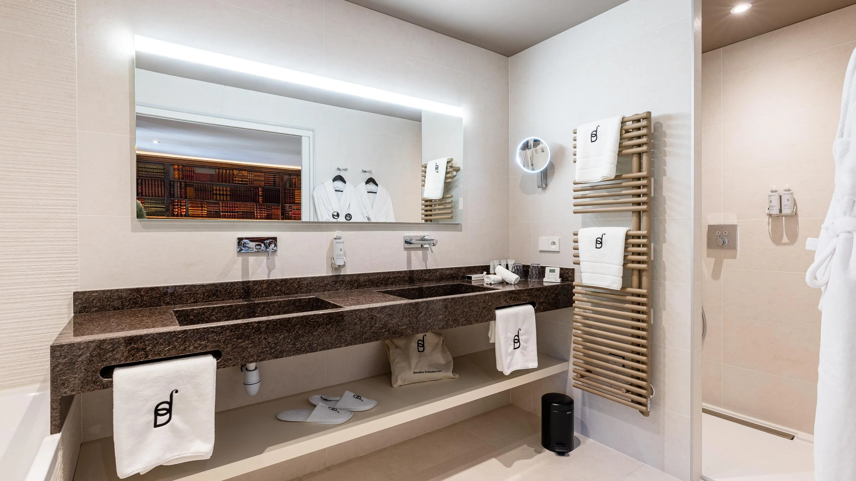 Modern bathroom with double sink, mirror, hanging towels and robes, and soap holder on the wall