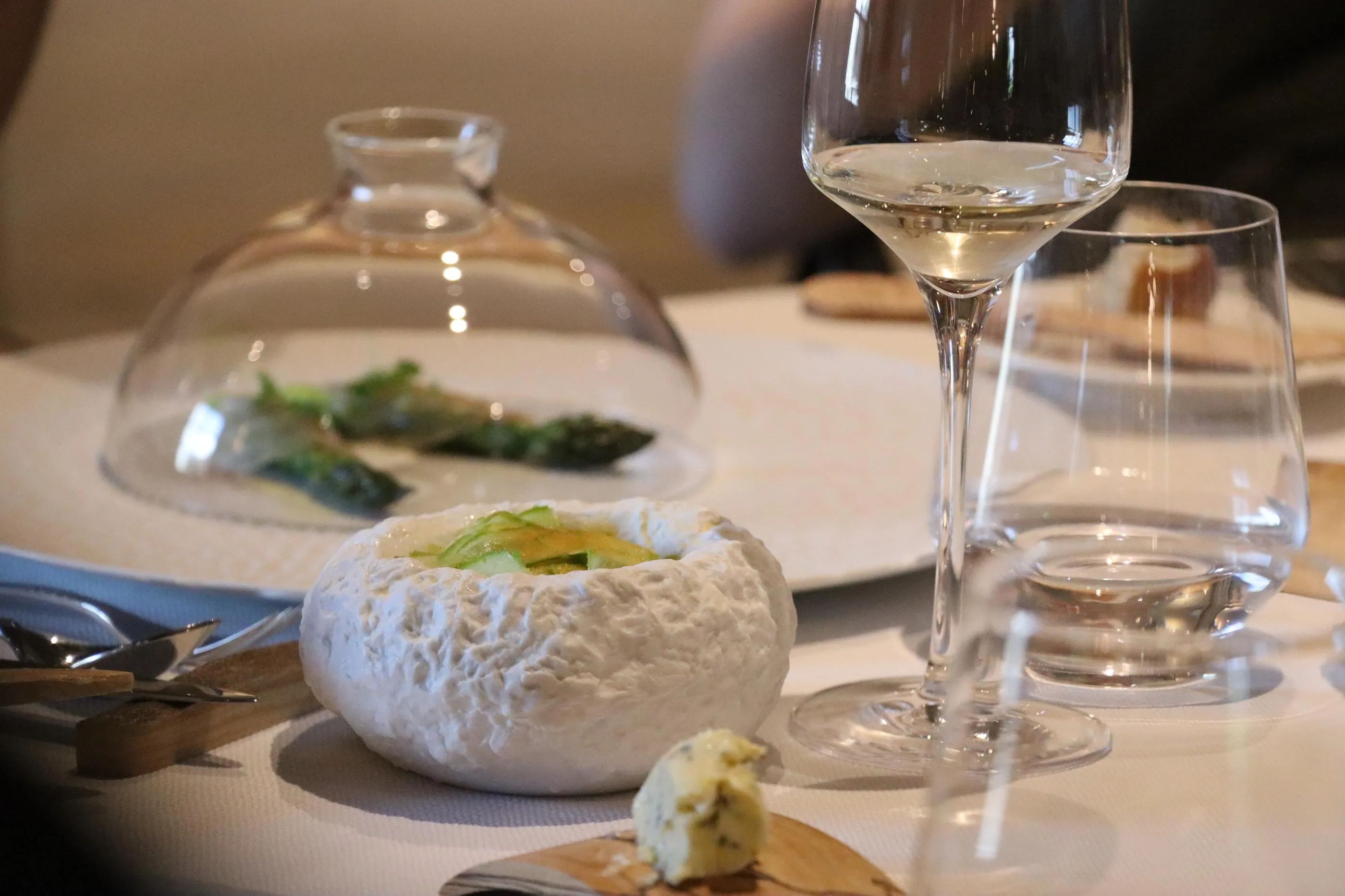 Un verre de vin blanc à moitié rempli et une assiette avec une boule de fromage blanc garnie de tranches d'avocat sur une table