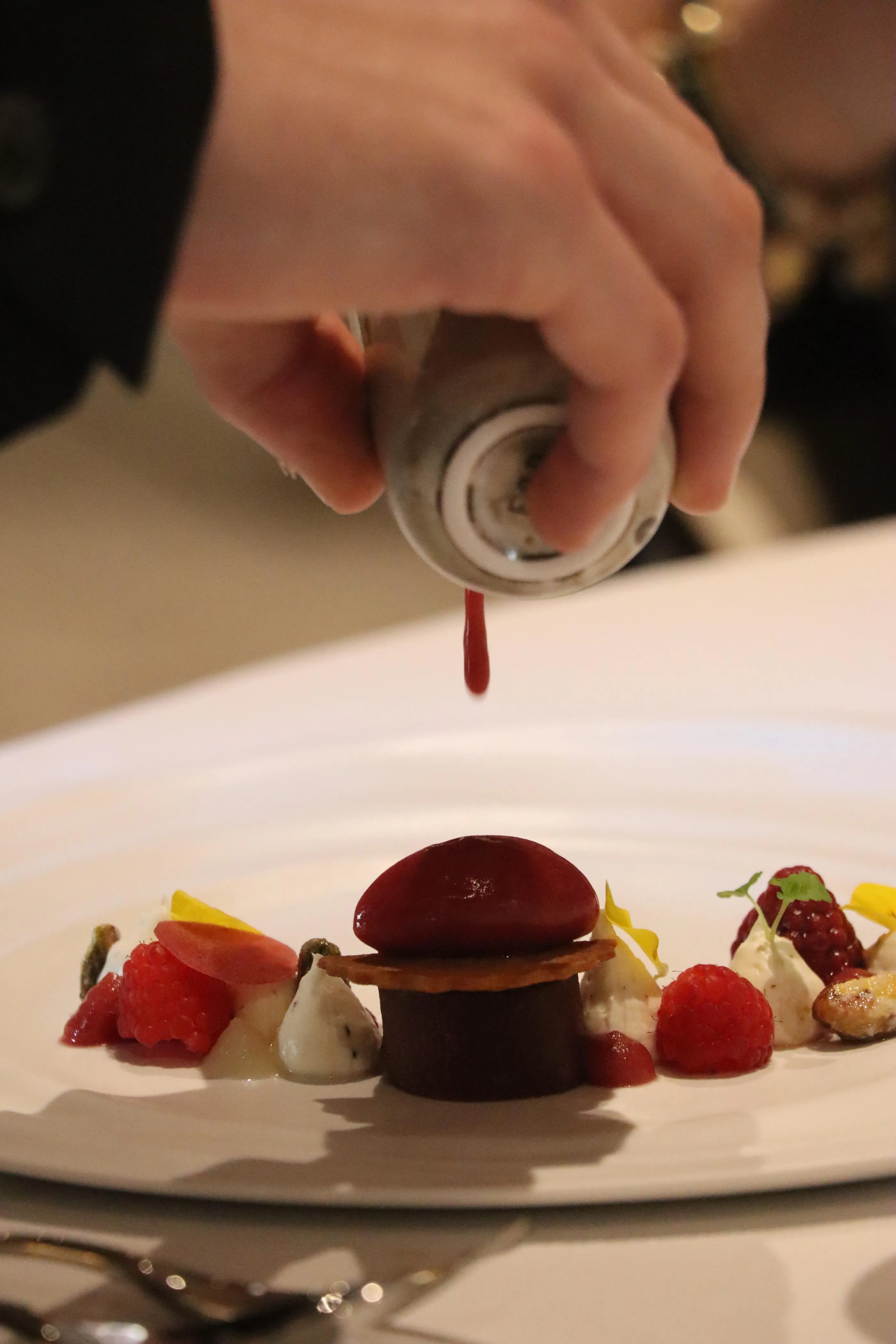 Une personne tient un tube à pâtisserie et décore un dessert composé de fruits et de garnitures sur une brochette